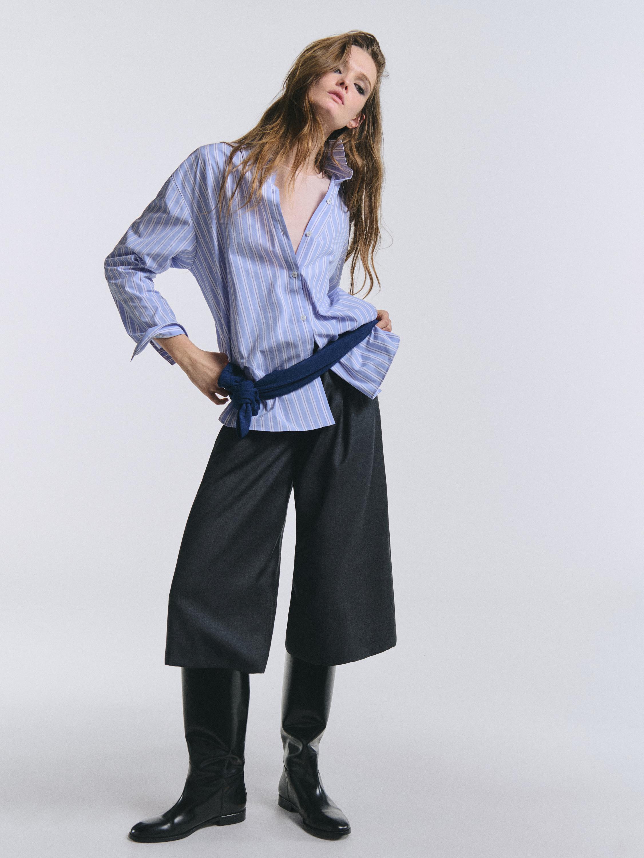 طقم قميص مخطط باللون الأزرق وشورت برمودا رمادي بكسرات، جزمة سوداء عالية.