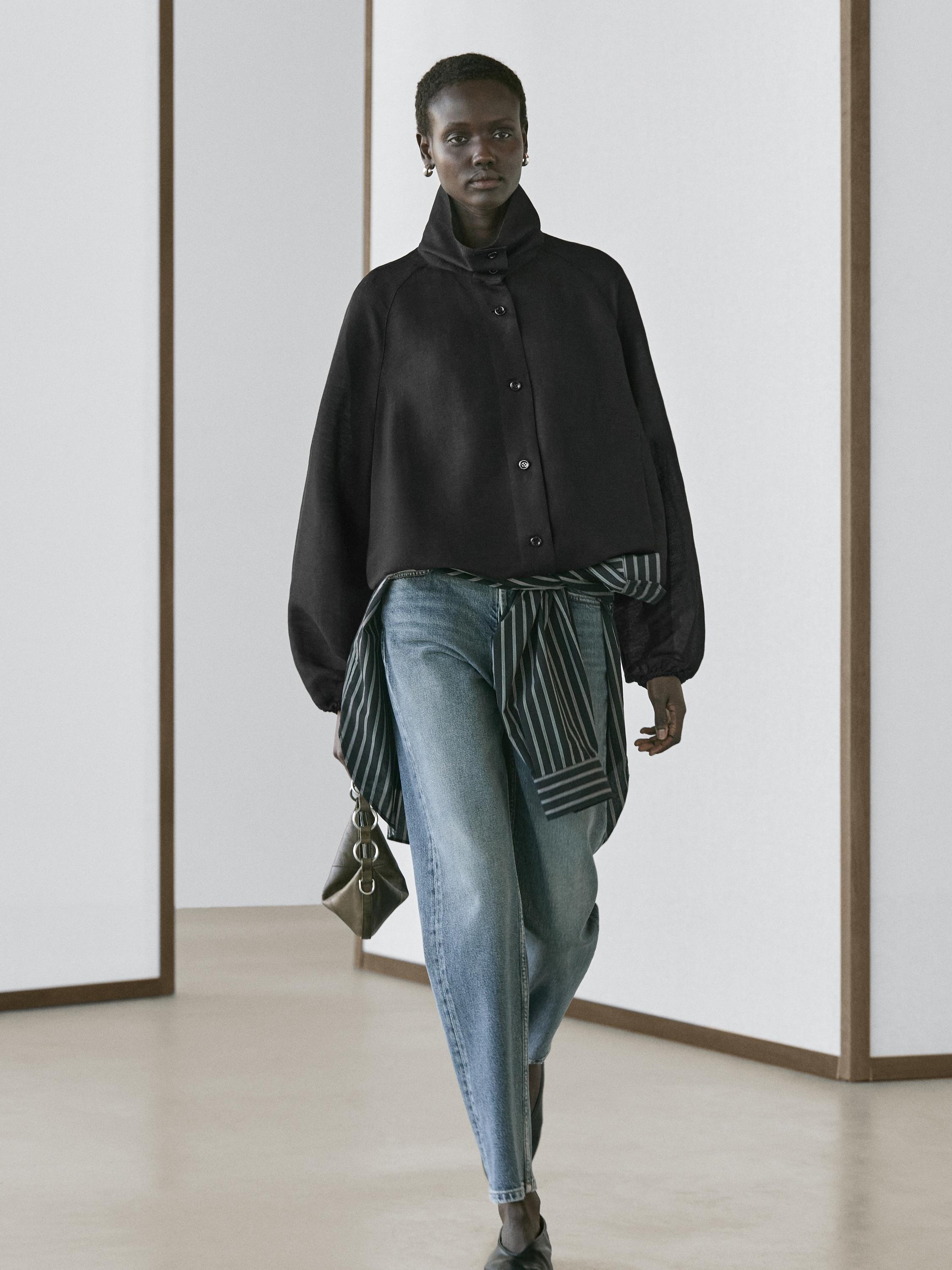 Conjunto de chaqueta bomber negra con botones, jeans azules y bufanda de rayas.