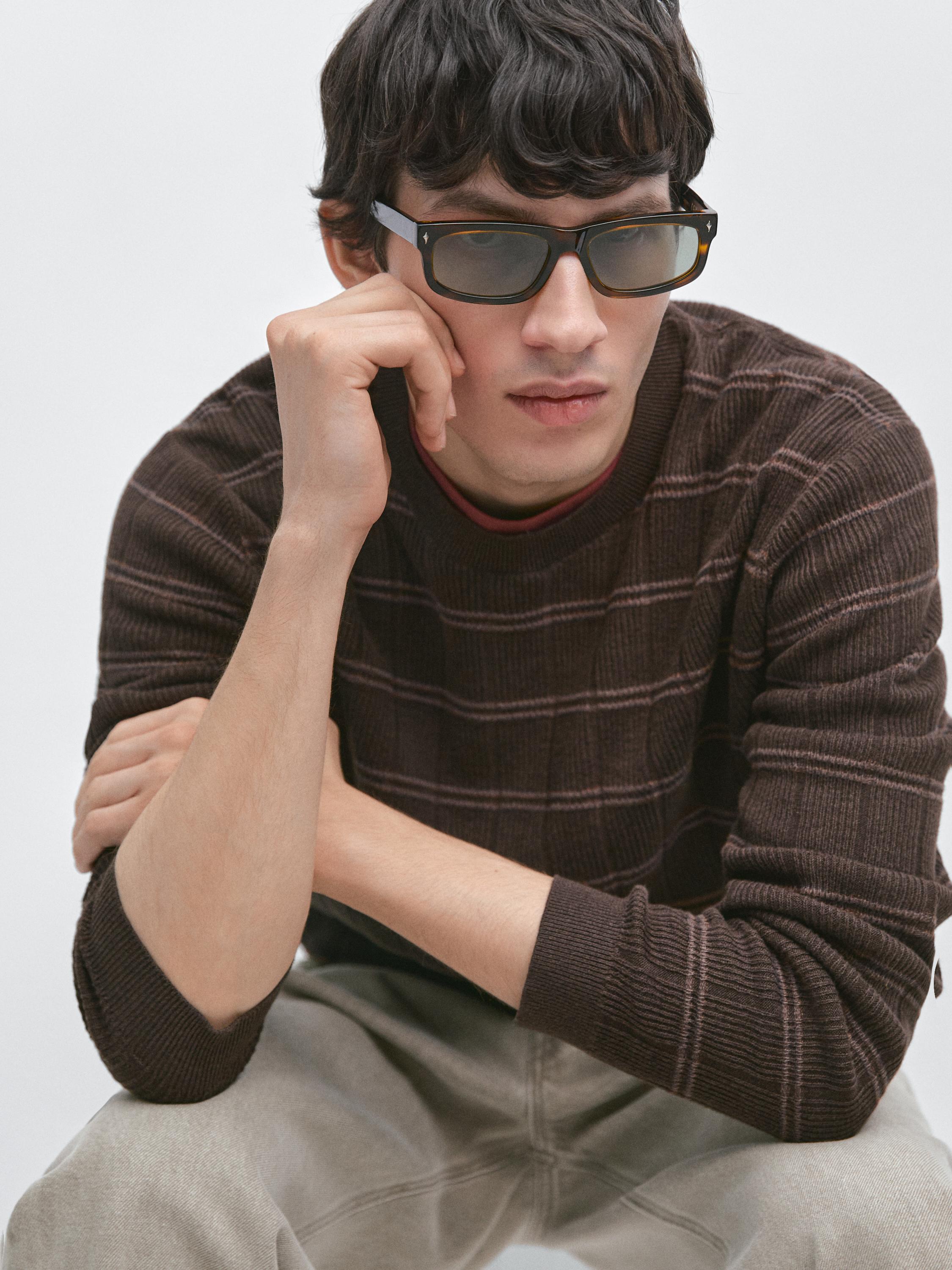 Plano médio de camisola castanha com riscas finas horizontais e gola redonda.