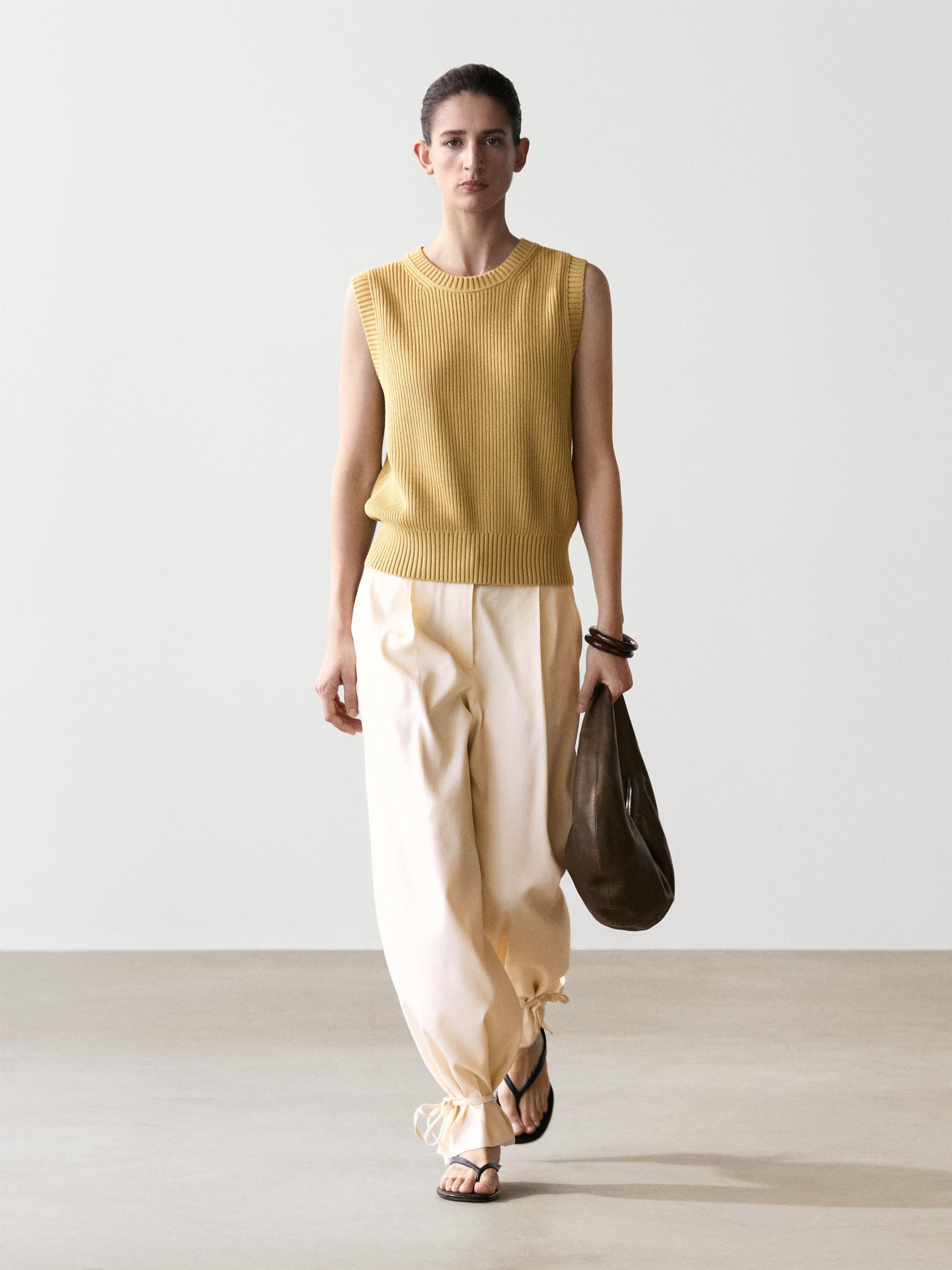 Ensemble gilet sans manches verdâtre et pantalon beige avec des liens aux chevilles.