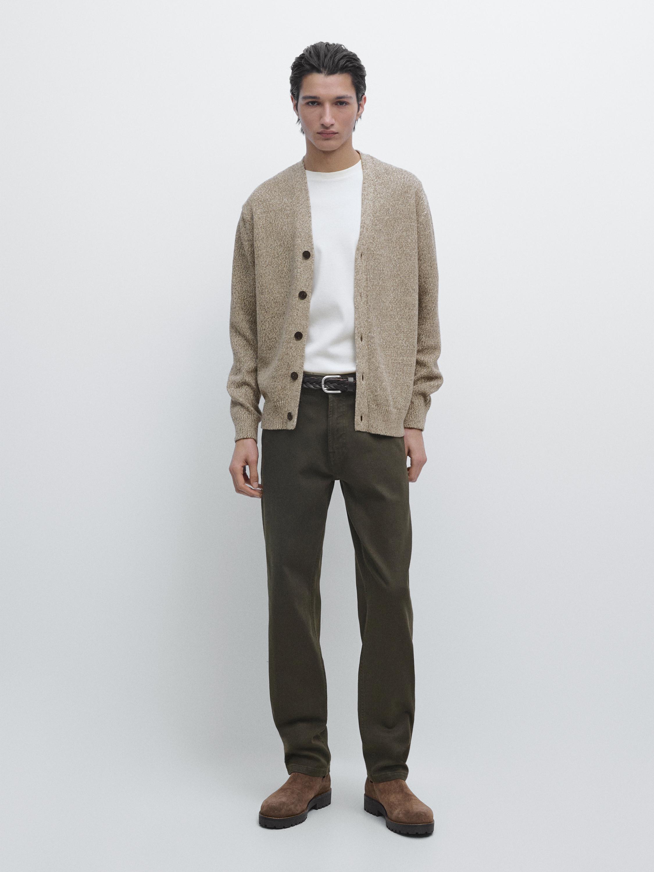 Conjunto de cárdigan beige con botones, playera blanca, pantalones verde oscuro y botas marrones.