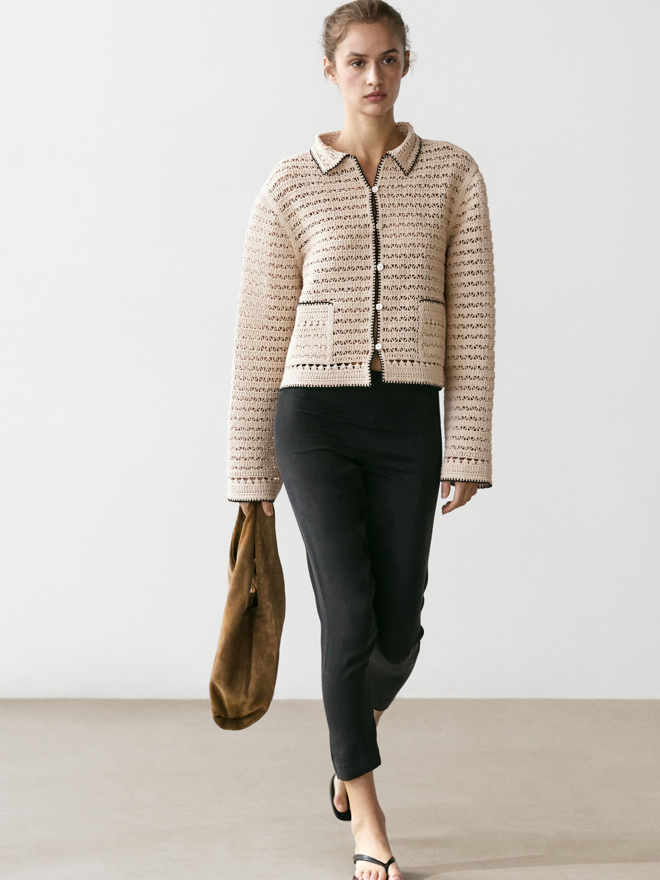 Ensemble veste beige en crochet avec poches avant et pantalon noir ajusté.