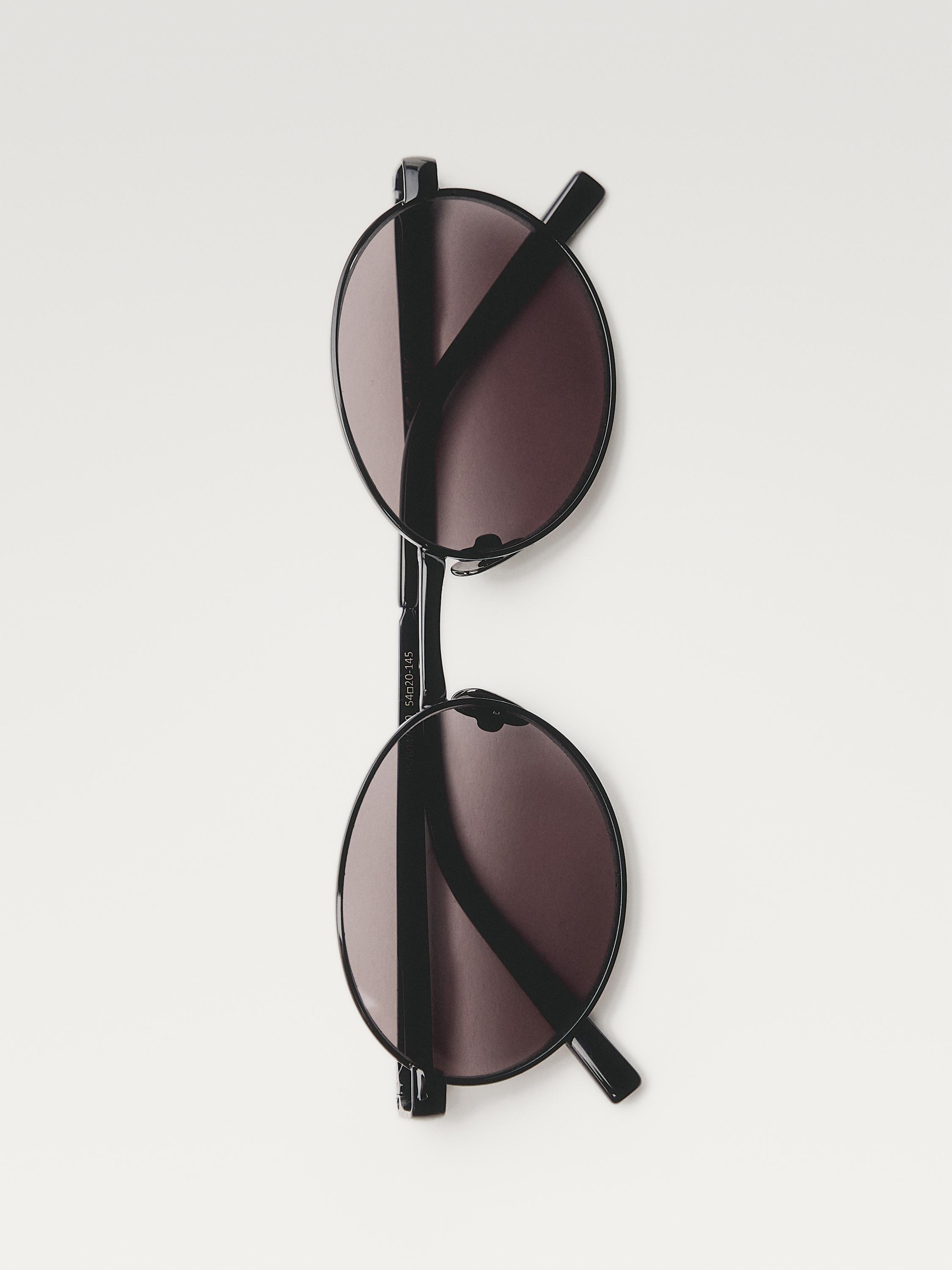 Vista frontal de lentes de sol negros con lentes redondas escuras e hastas delgadas. Dimensións: 54-20-145 mm.