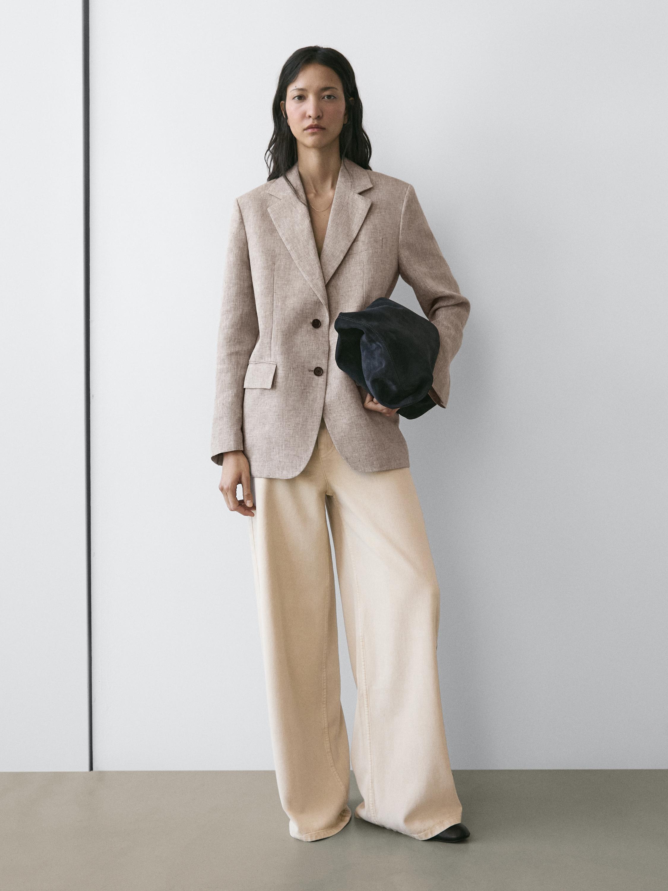 Bộ blazer màu be có ve áo và nút tối màu, quần ống rộng màu kem và túi xách tối màu.