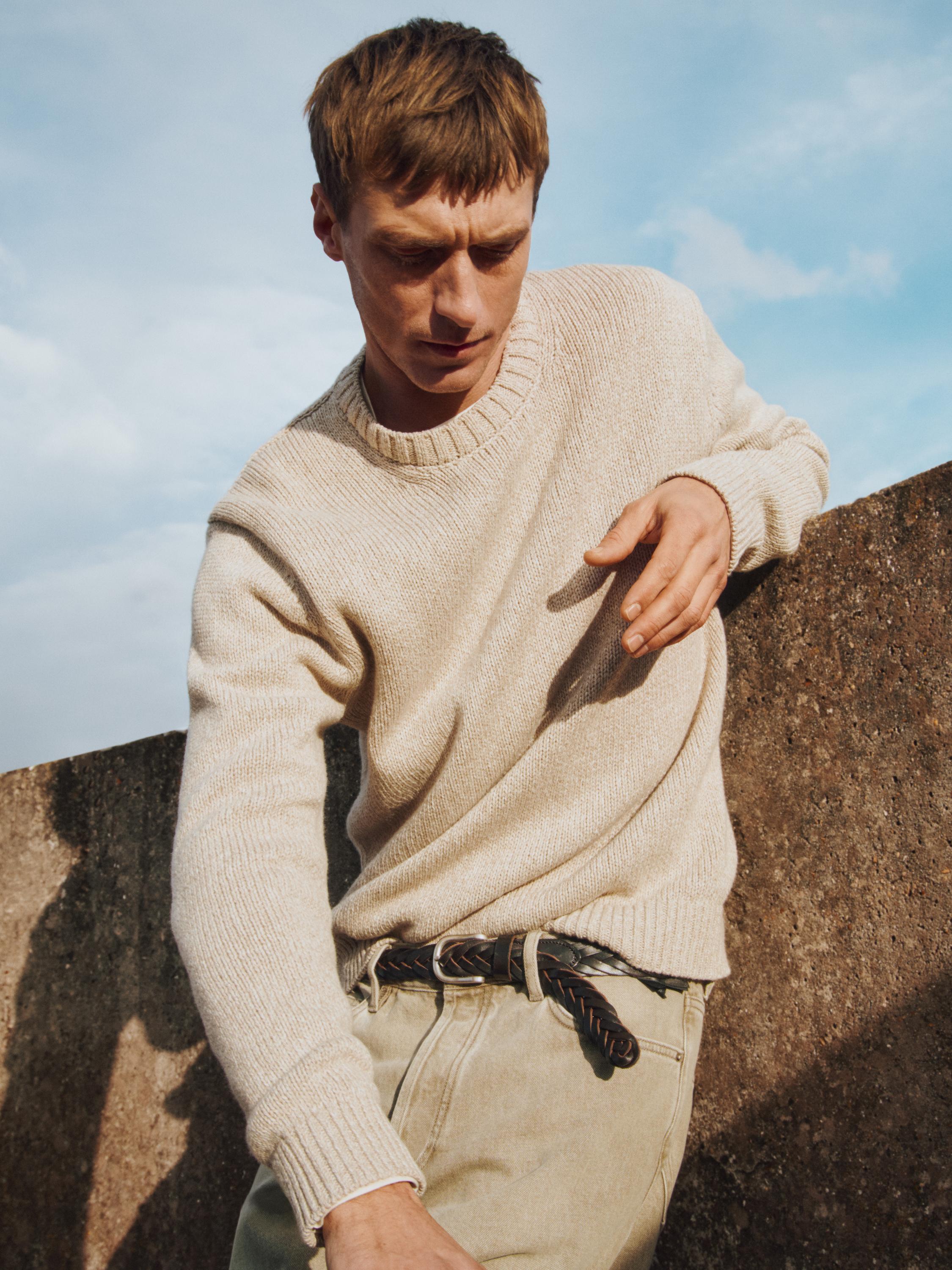 Крупный план бежевого вязаного джемпера с круглым вырезом и длинными рукавами.