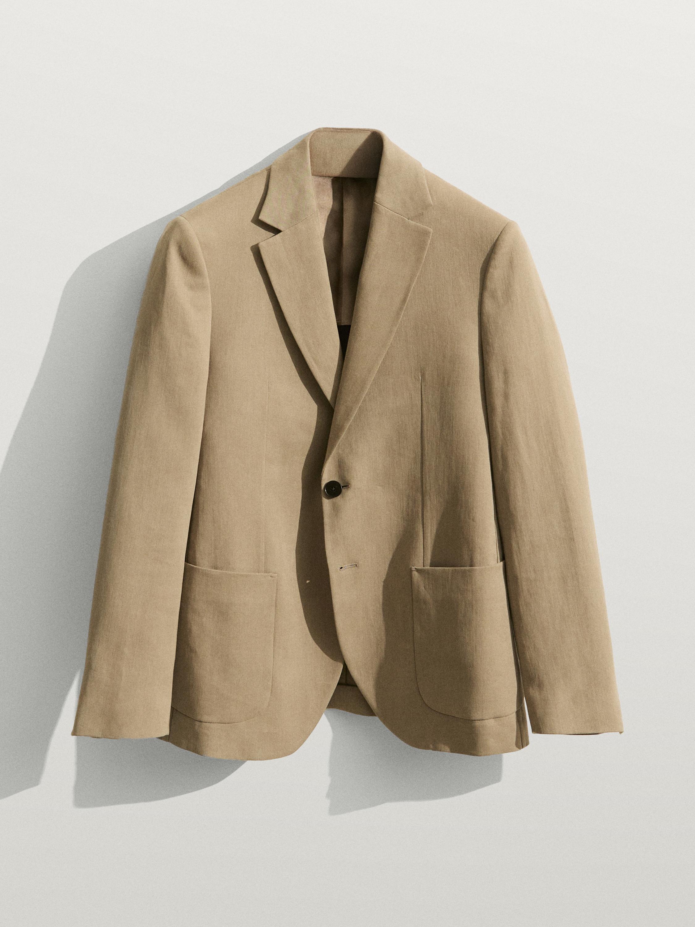 Vista frontal de americana beige con solapa de muesca y un botón, bolsillos delanteros grandes.