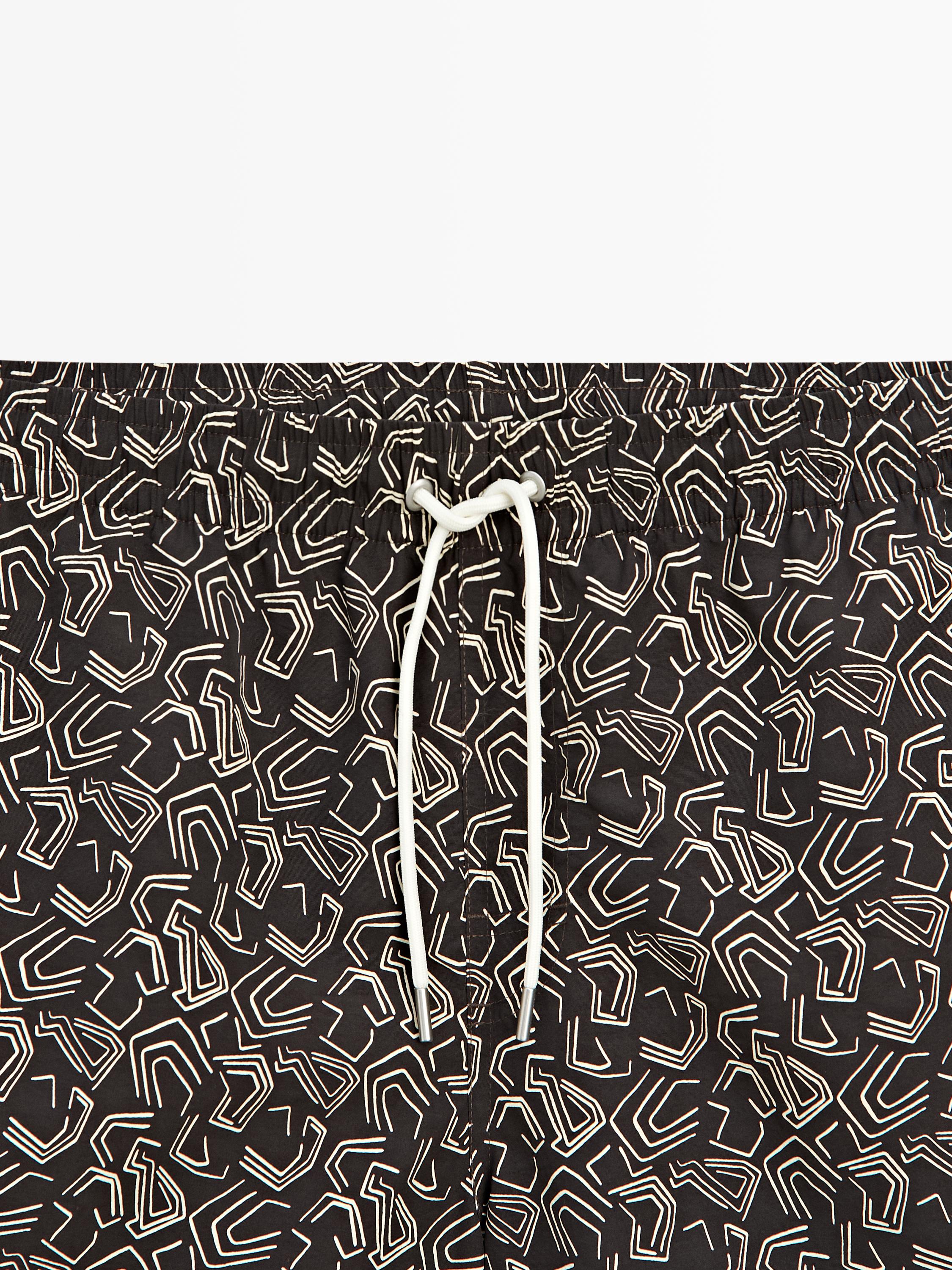Taillendetail einer braunen Badehose mit weißem geometrischem Muster und weißem verstellbaren Kordelzug.