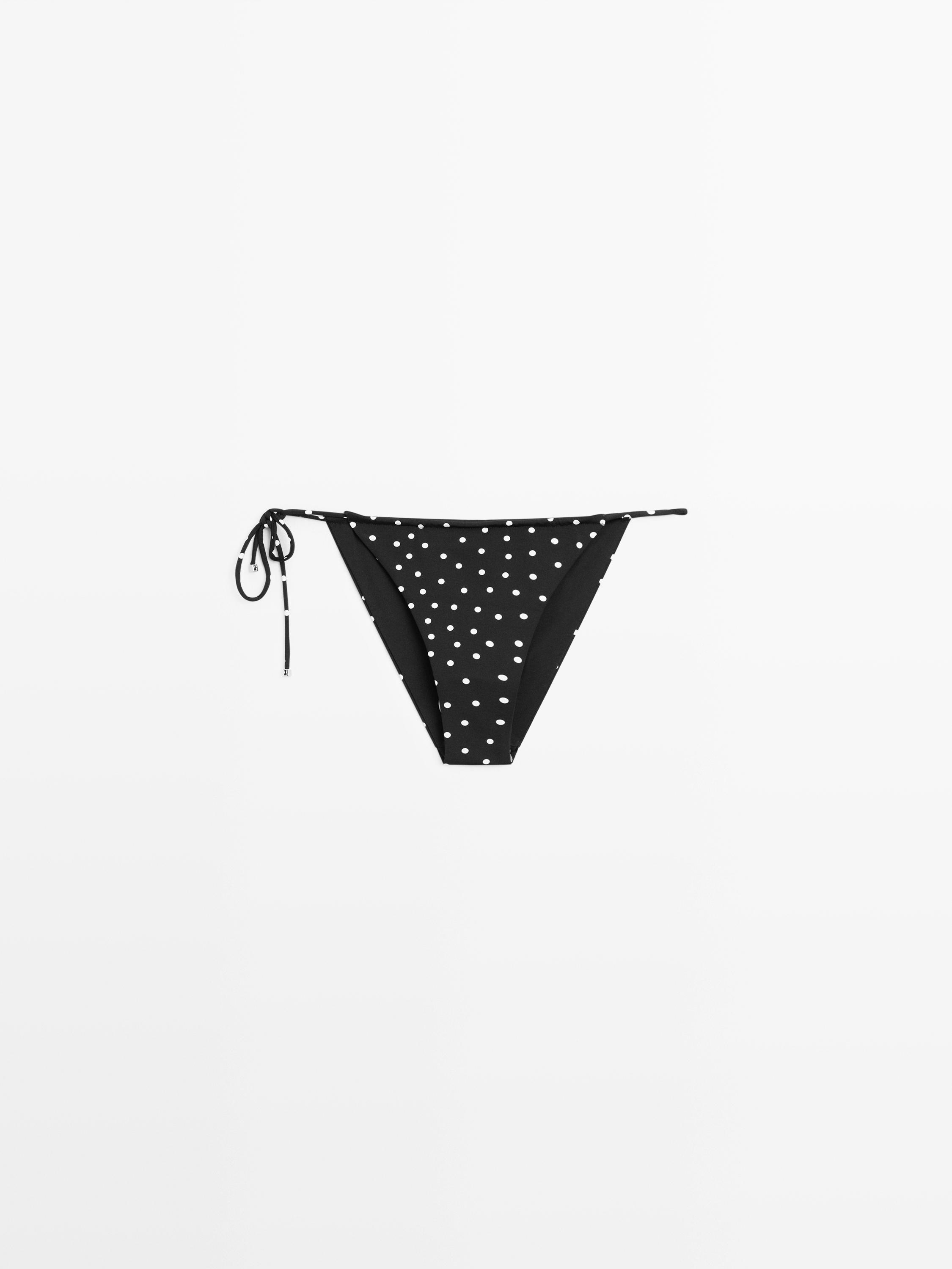 Vista frontal de bikini negro con estampado de lunares blancos y lazos laterales ajustables.