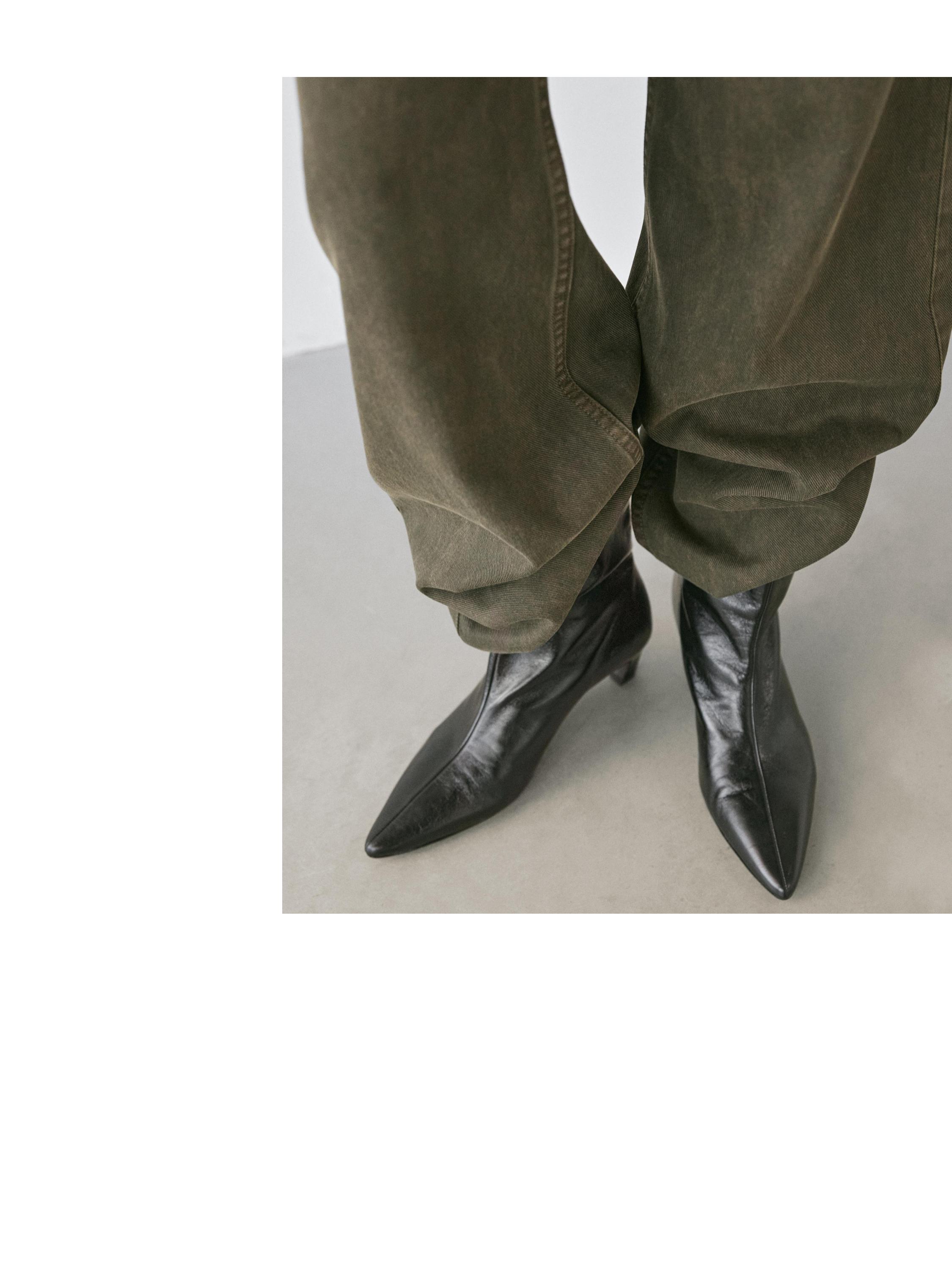 Plano medio de pantalones caqui oscuro de pierna ancha con botas negras puntiagudas visibles.