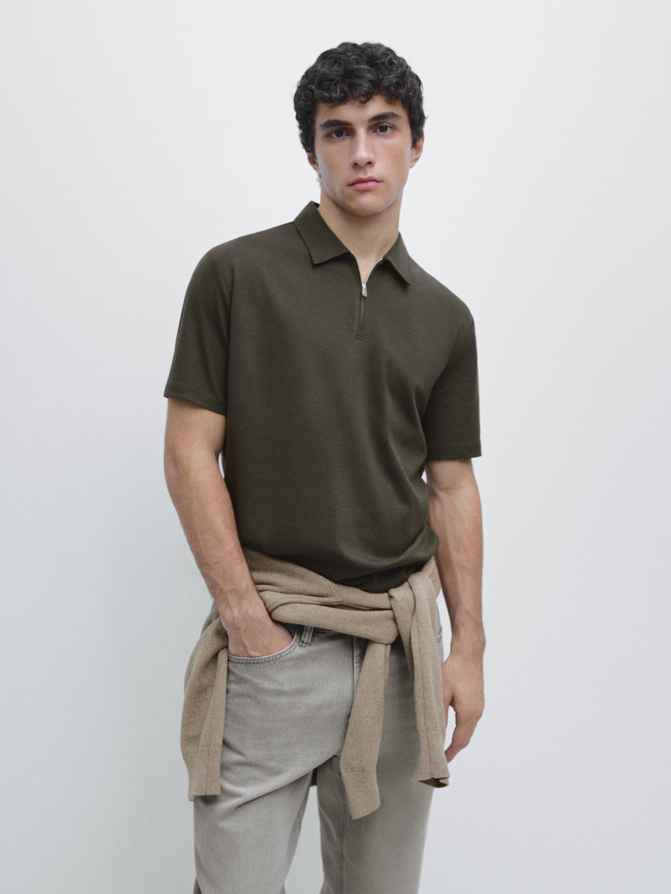 Conjunto de polo verde oscuro de manga corta con cremallera y pantalones grises. Suéter beige atado a la cintura.