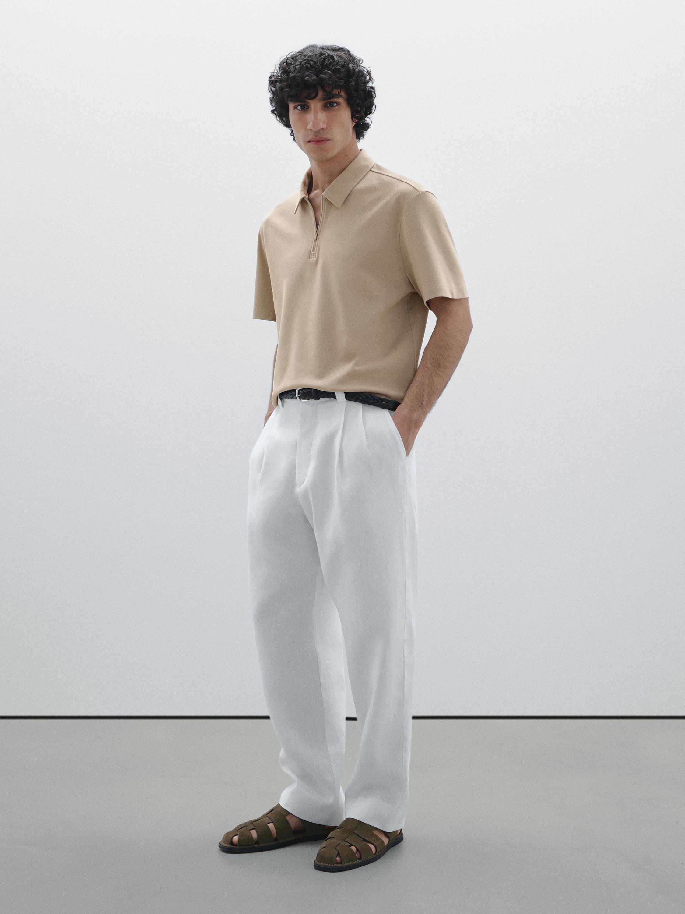 Ensemble polo beige à fermeture éclair, pantalon blanc ample et sandales marron.