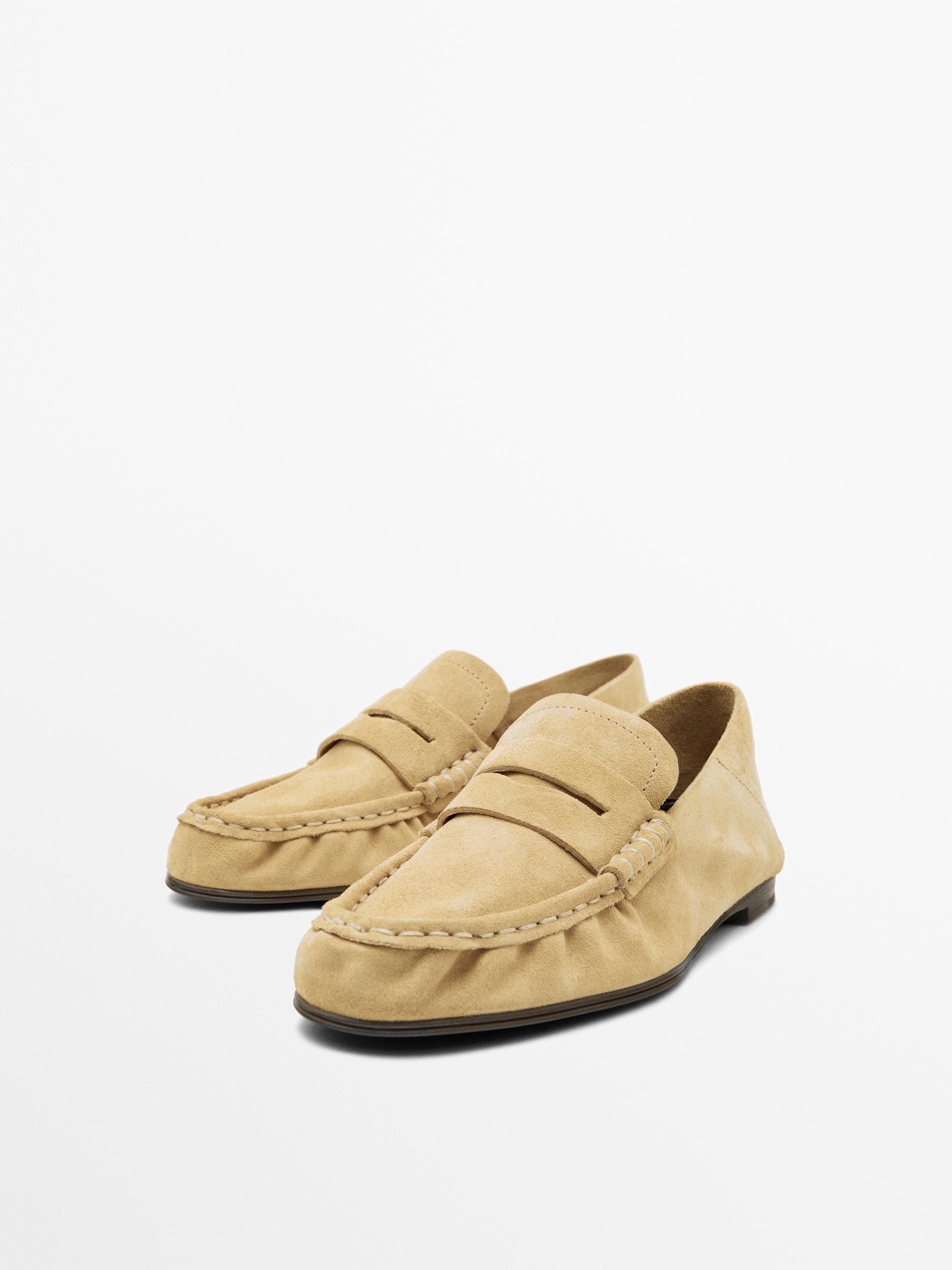 Vista frontal de mocasíns beis con costuras visibles e sola plana.