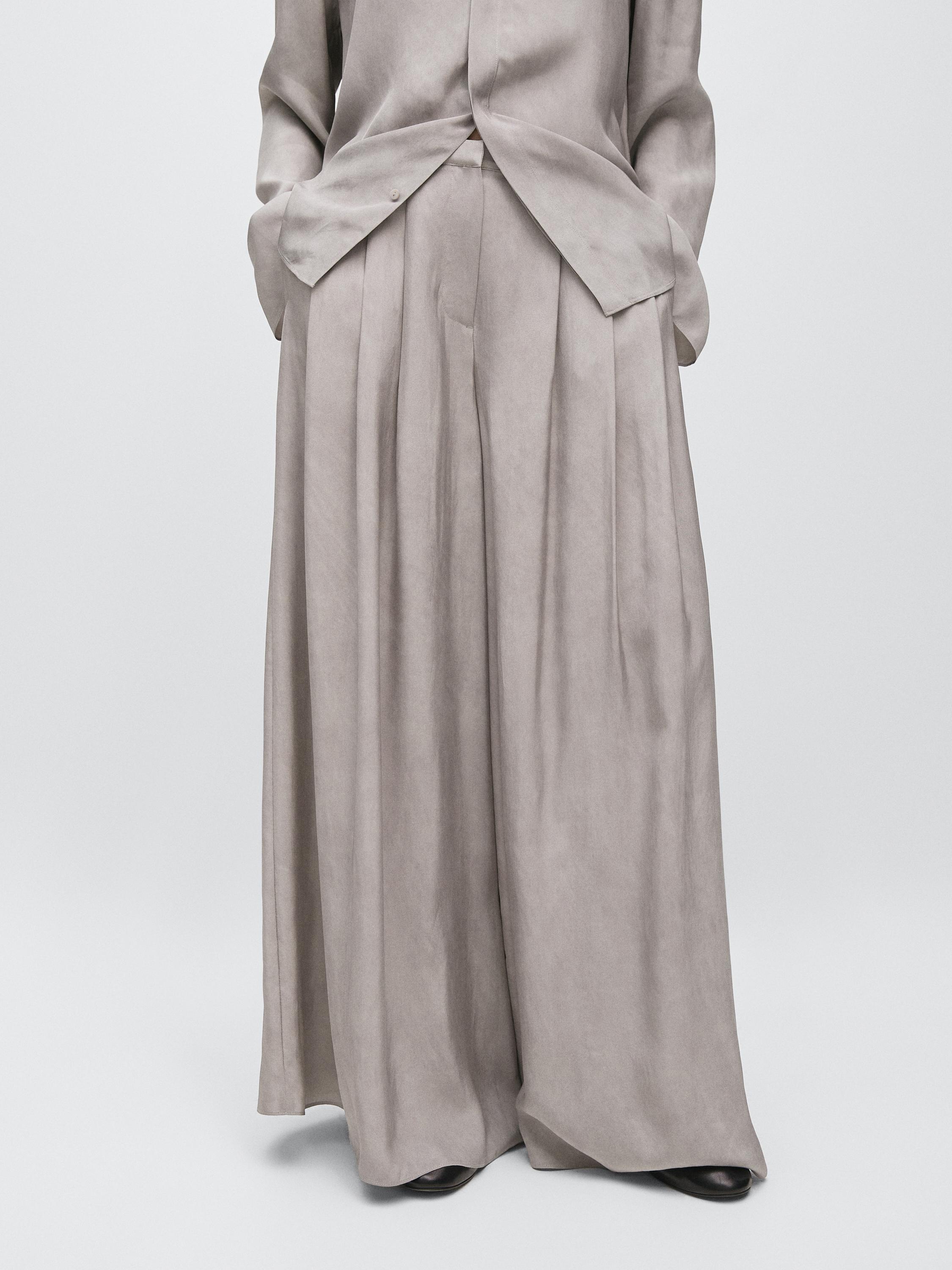 Mid-shot of gray pants with pleats and side pockets.