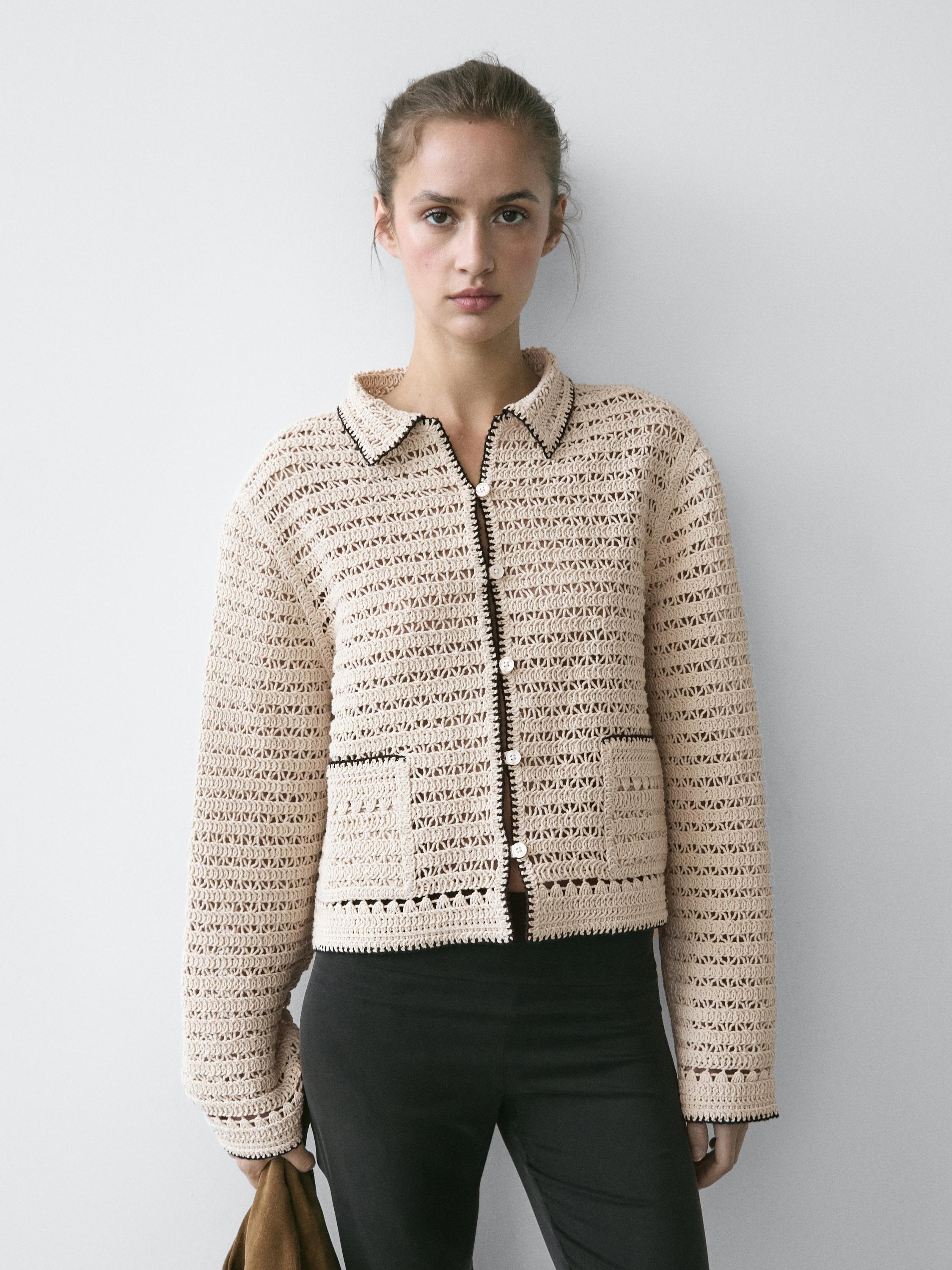 Beige cropped crochet jacket set with front buttons and front pockets, paired with dark pants.