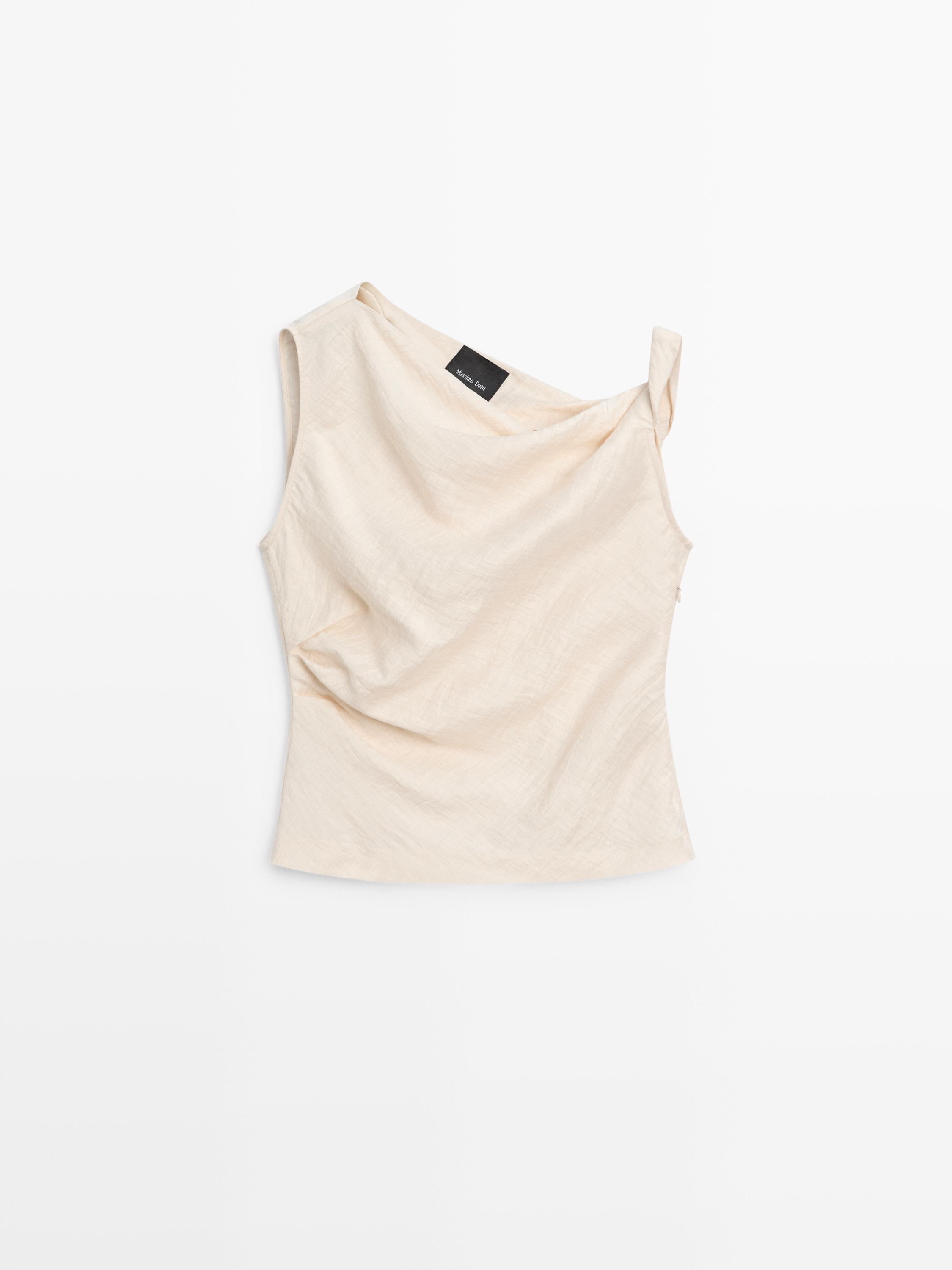 Front view of a sleeveless beige top with an asymmetrical neckline and draped detail.