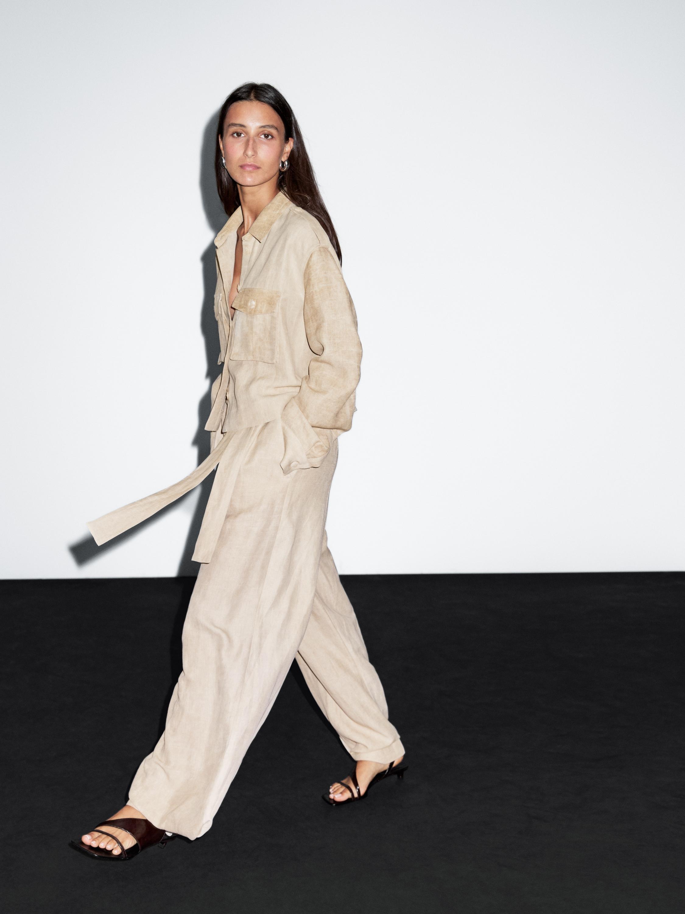 Ensemble composé d'une chemise couleur sable avec poches avant et ceinture, assortie à un pantalon large et des sandales noires.