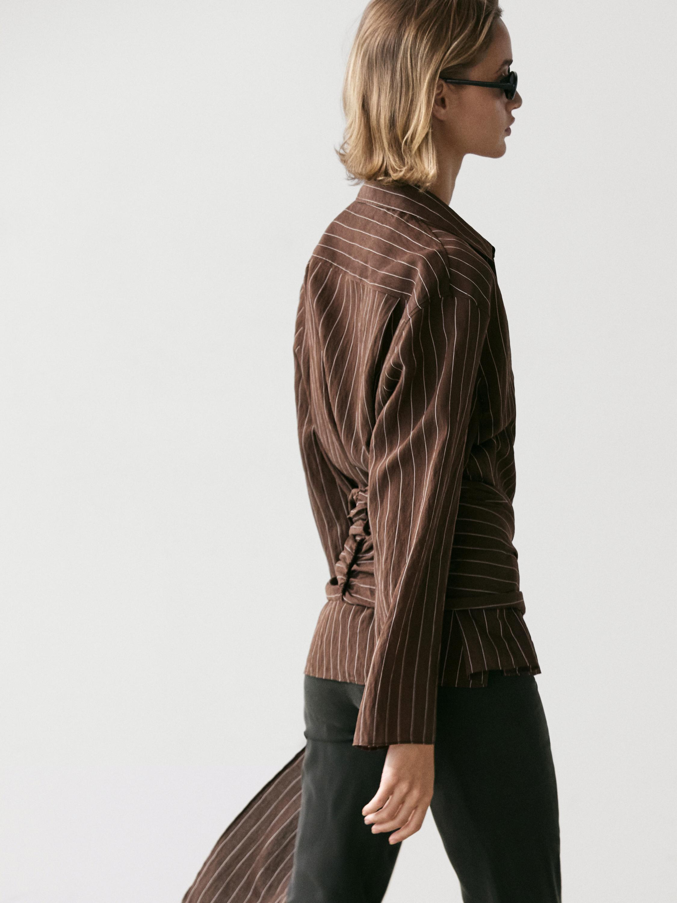 Plano medio de camisa café a rayas con detalle de pañuelo en la espalda, mangas largas y ajuste lateral.