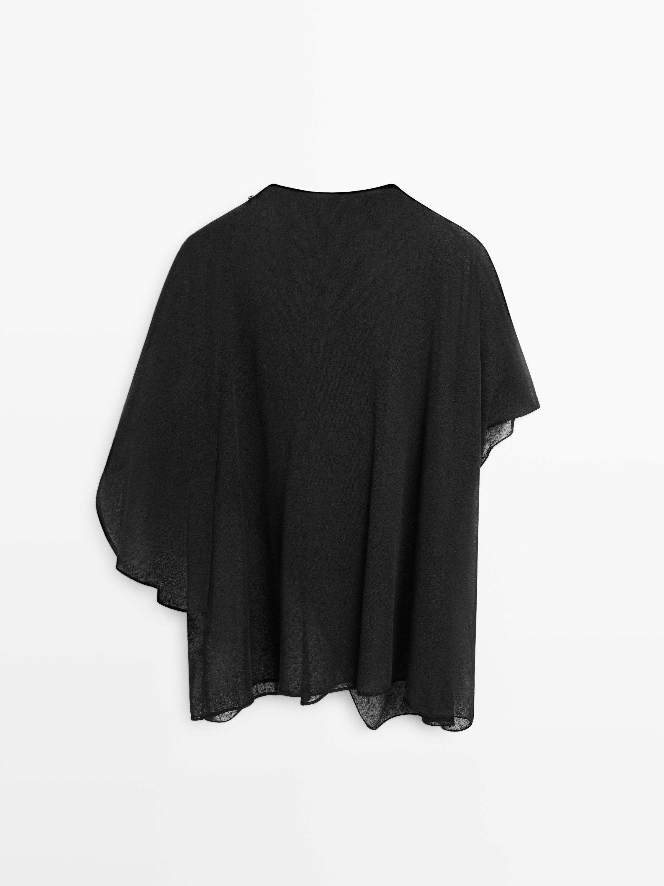 Vista posterior de blusa preta de manga comprida com corte assimétrico e caimento fluido.