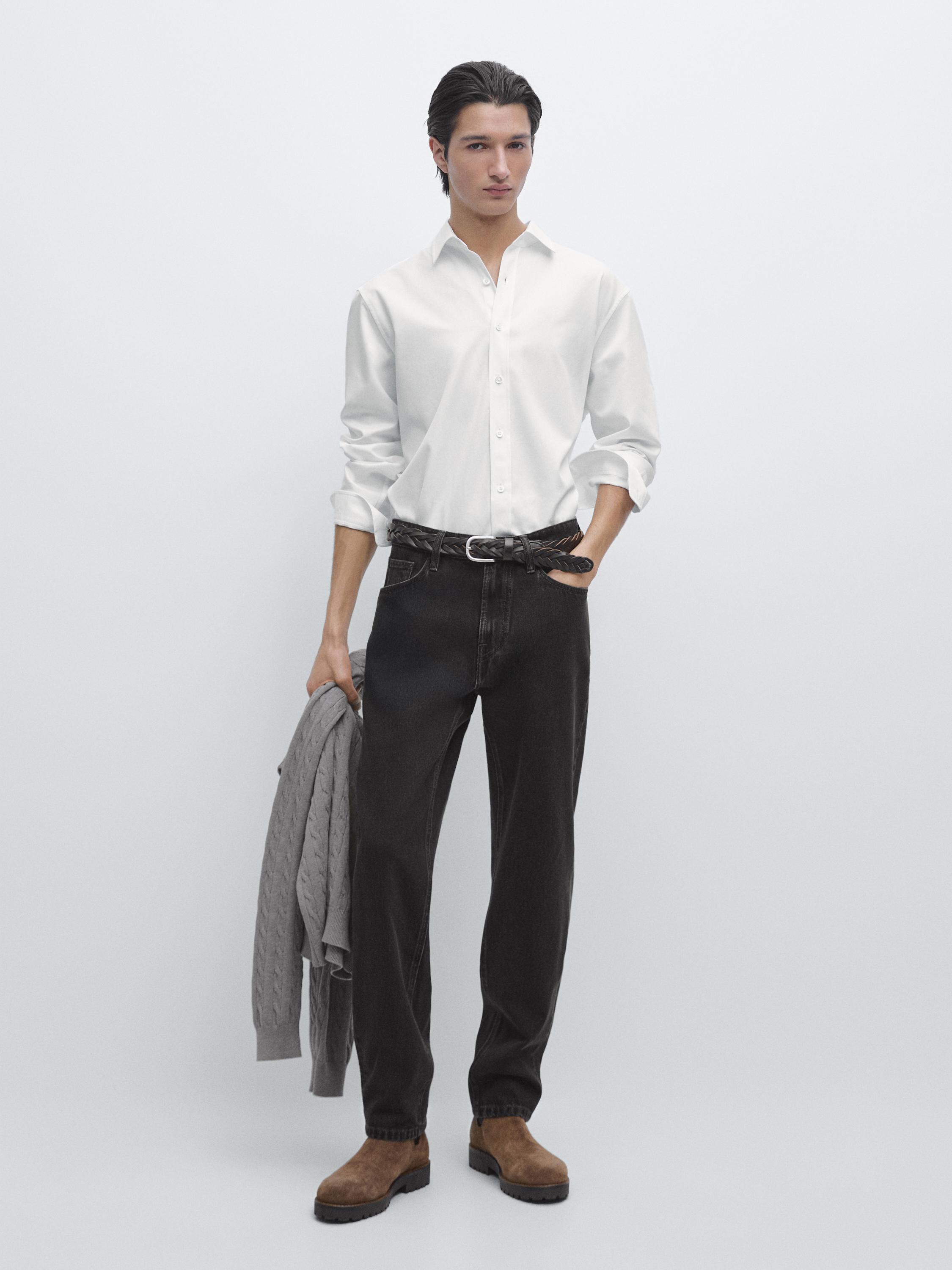 Completo di camicia bianca a maniche lunghe, pantaloni neri e stivali marroni.