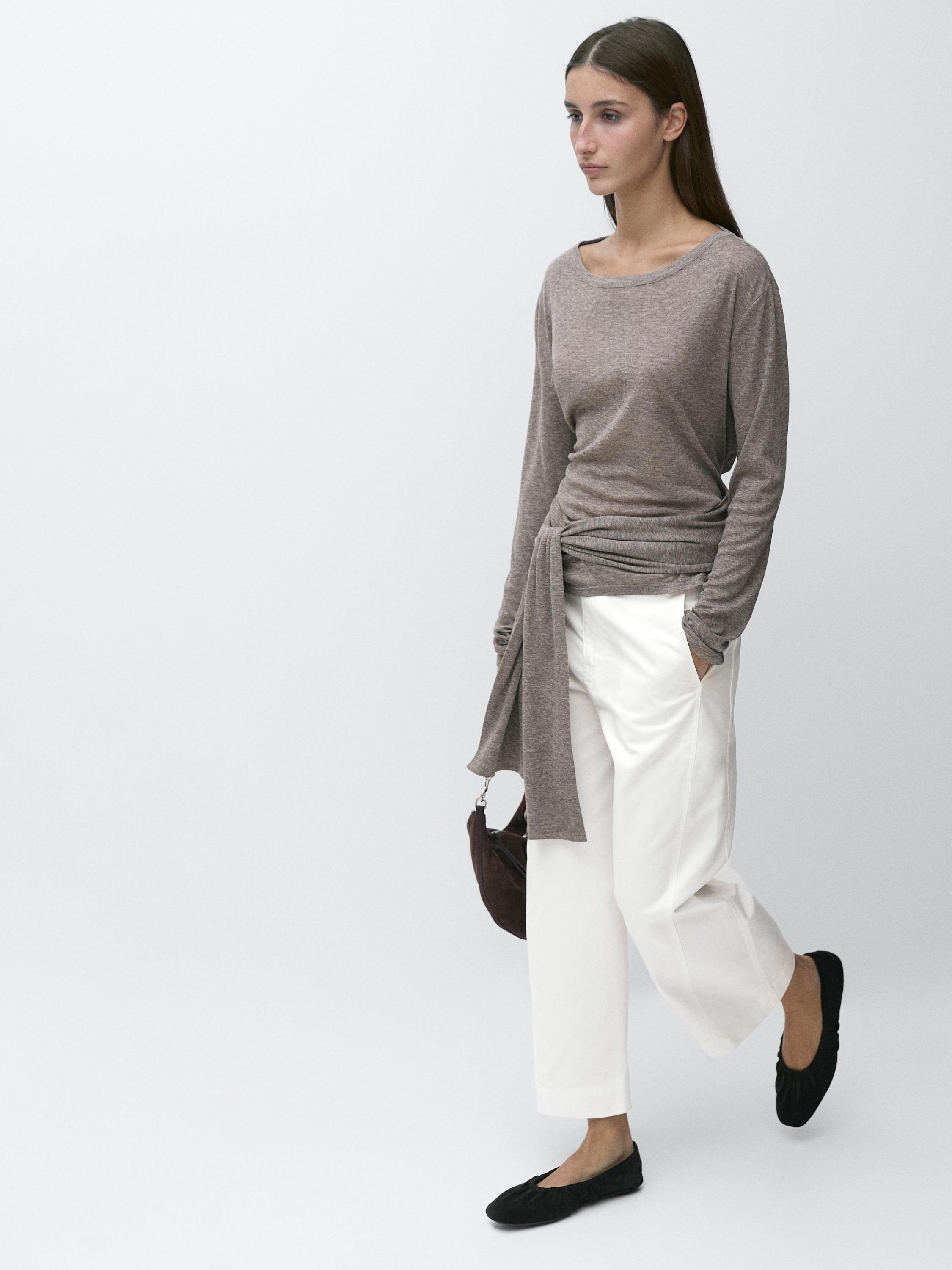 Bộ quần ống rộng màu trắng cạp cao dáng barrel fit có túi bên và áo blouse màu xám tay dài có thắt nút bên.