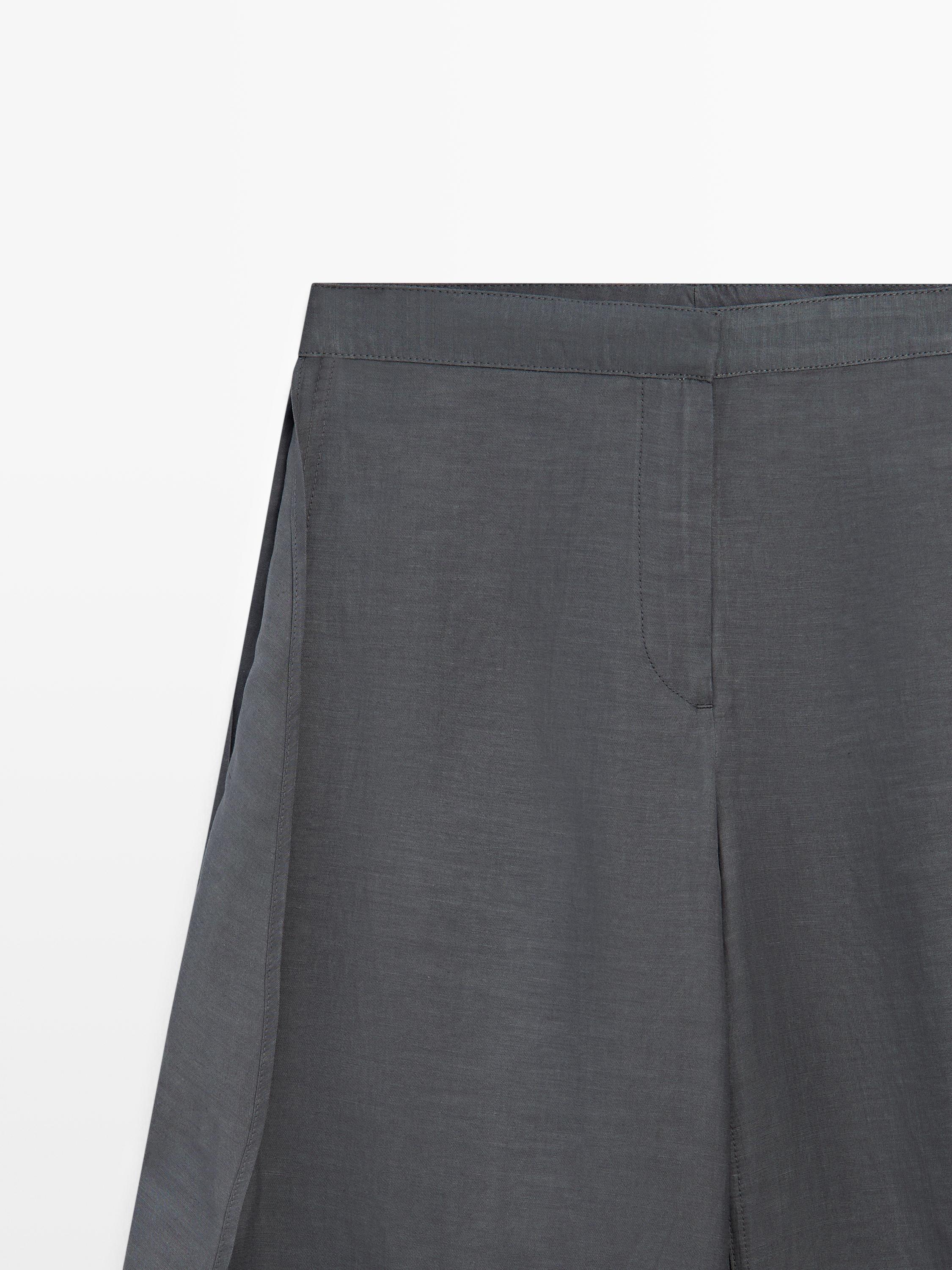 Plano medio de pantalón gris antracita con aberturas laterales y costuras visibles en la cintura.