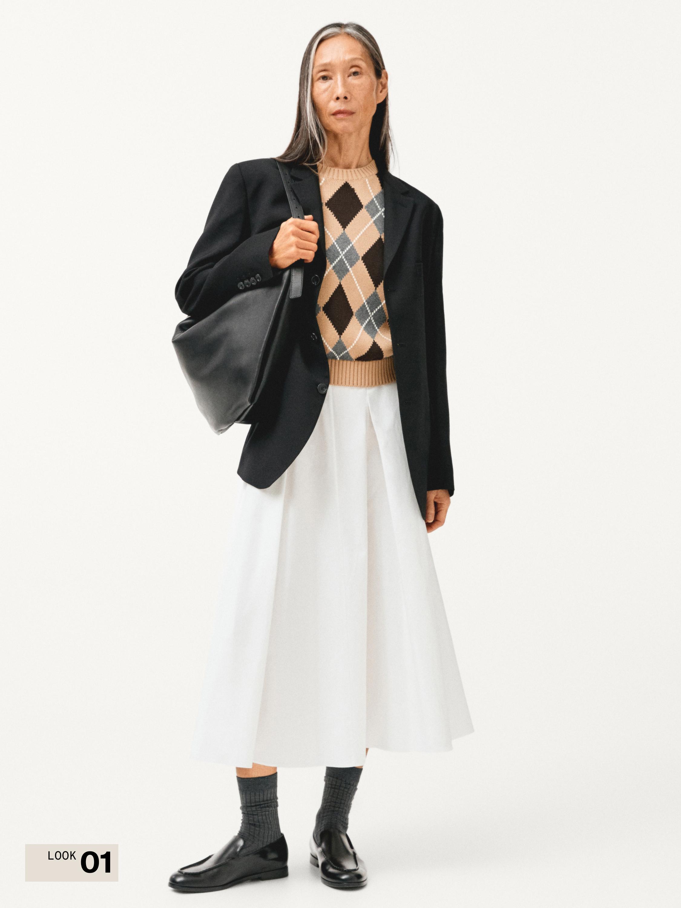 طقم بليزر أسود، سويتر بنقشة الماسات بيج وأسود، تنورة بيضاء متوسطة الطول، جوارب رمادية وأحذية سوداء.