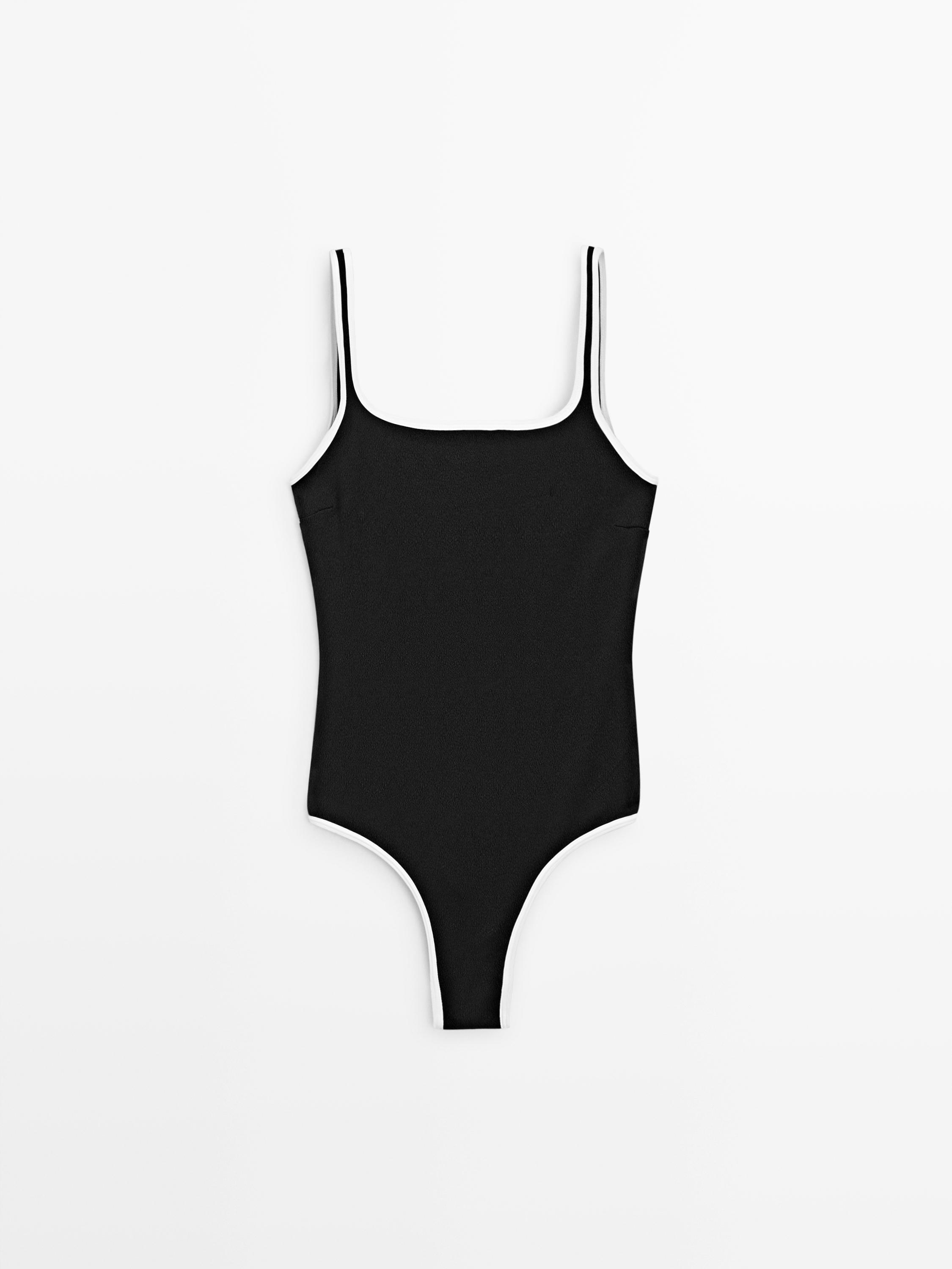 Vue de face d'un maillot de bain noir avec de fines bretelles et un liseré blanc au niveau du décolleté et sur les côtés.
