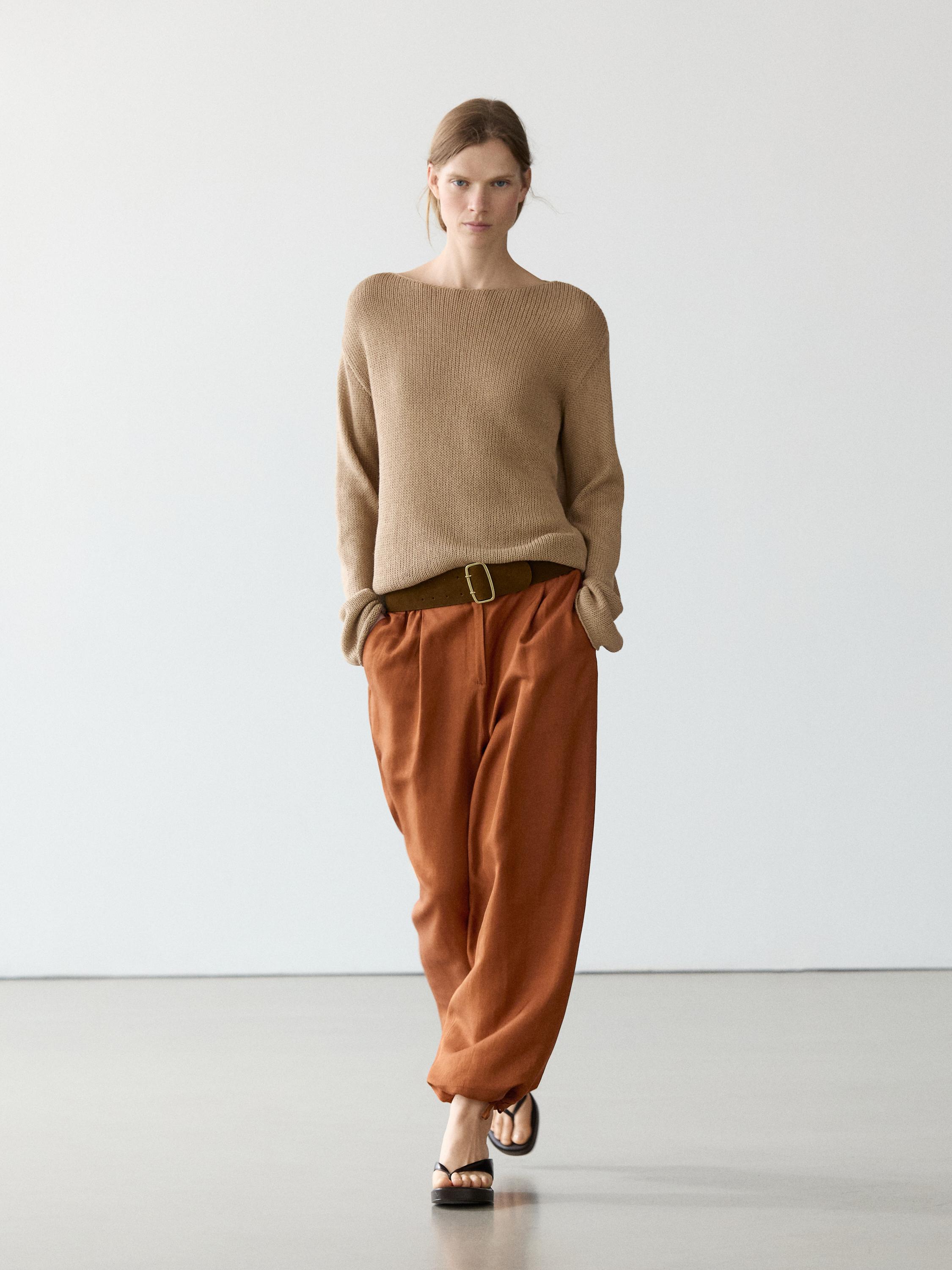 Beżowy sweter z dzianiny i pomarańczowe szerokie spodnie z wiązaniem i paskiem.