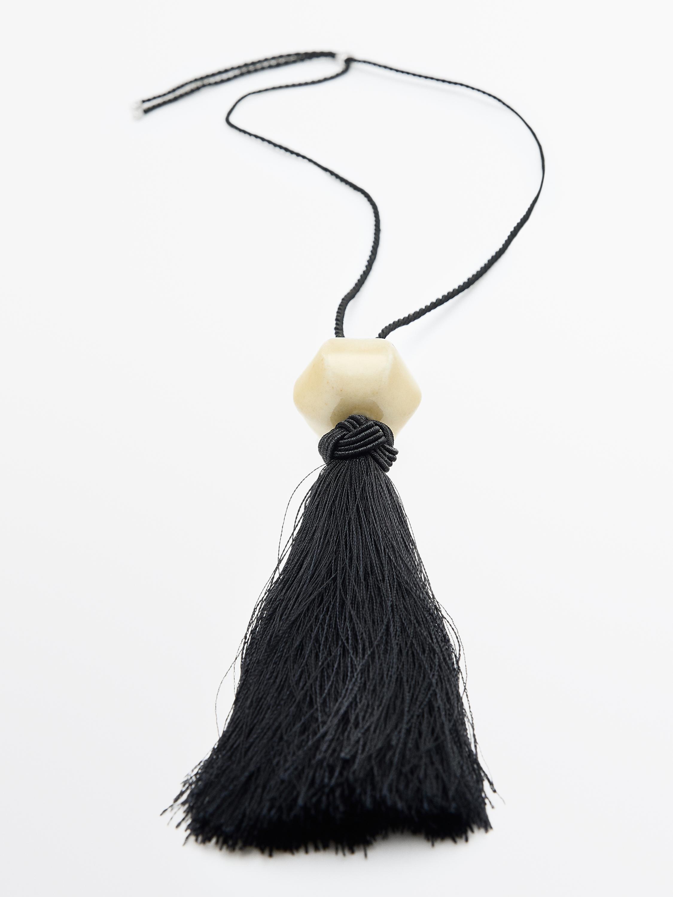 Black necklace with long tassel and geometric piece in beige color.