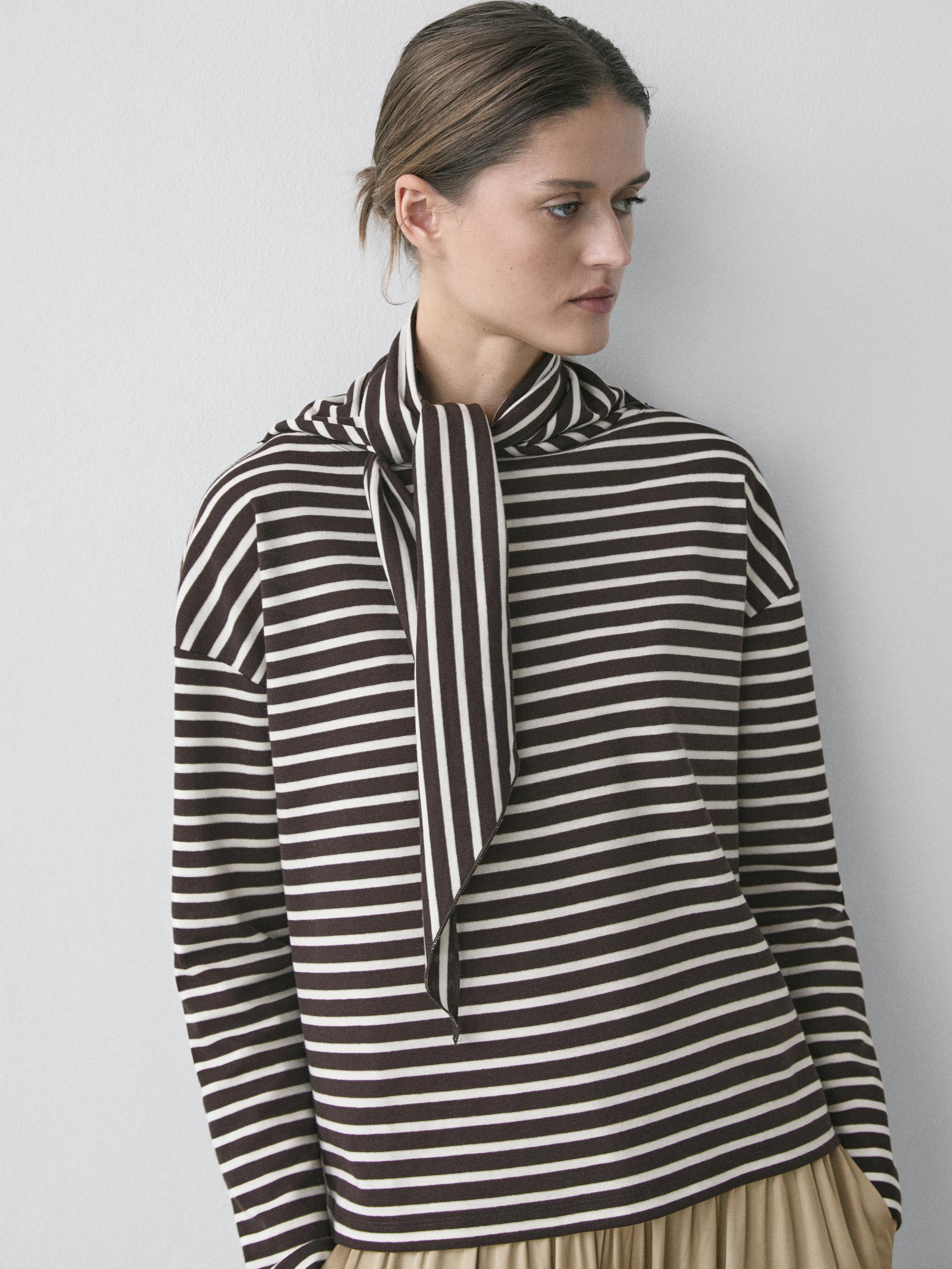 Plano medio de camiseta marrón de rayas con detalle de pañuelo en el cuello y mangas largas.