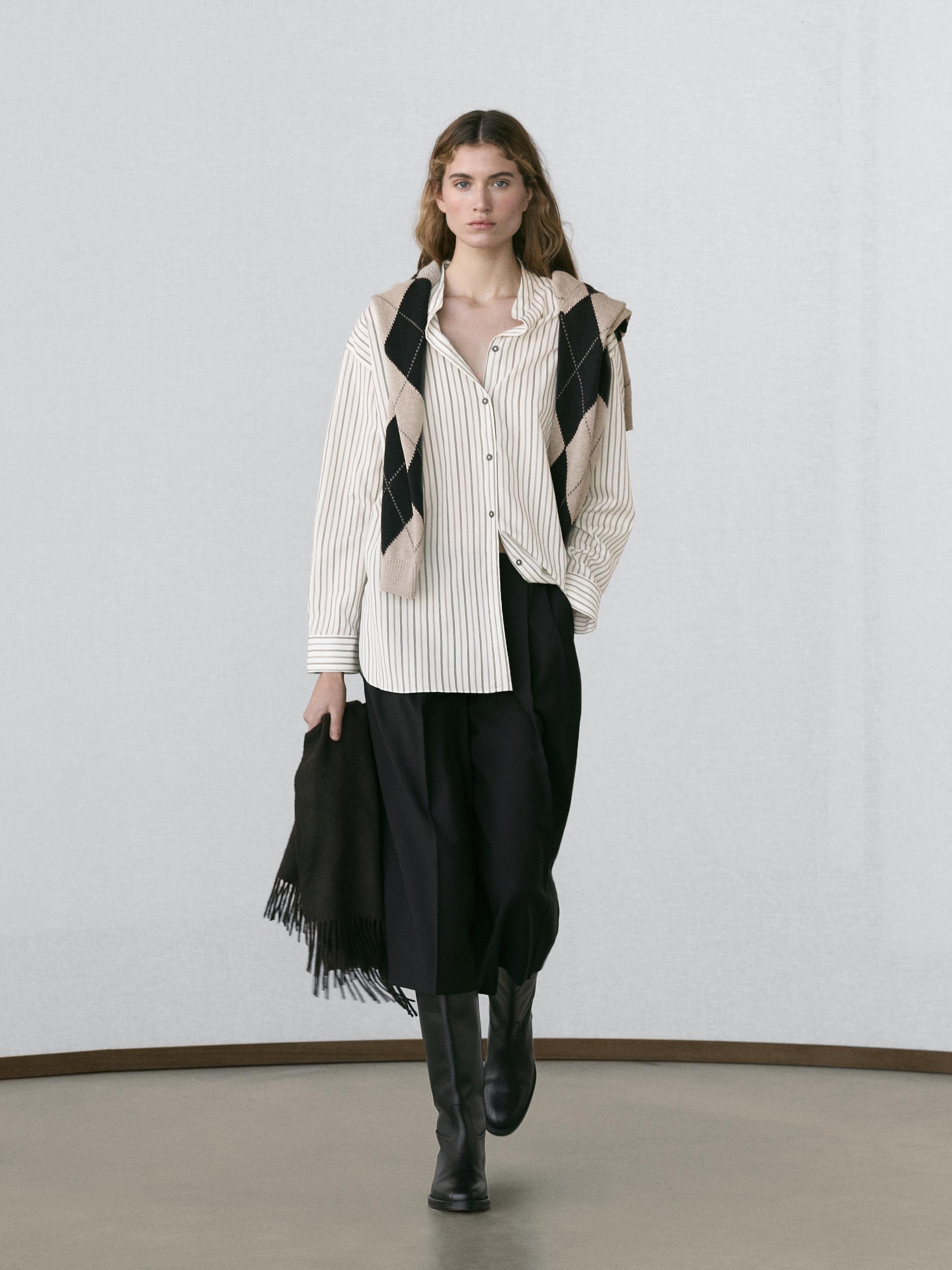 Conjunto de camisa a rayas blancas y negras, bermuda negra larga, botas negras y bufanda de rombos beige y negra.