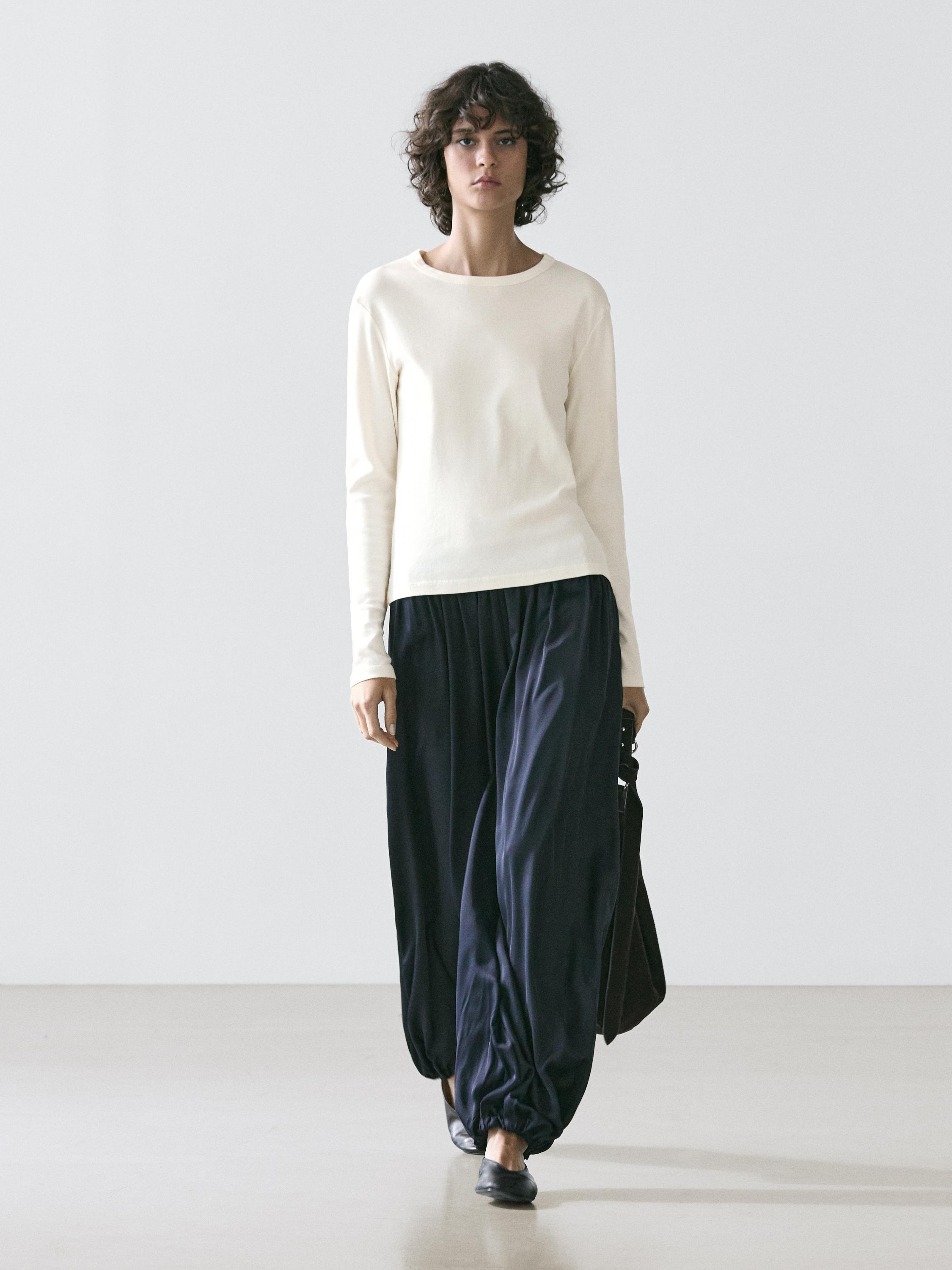 Conjunto de t-shirt crua de manga comprida e calças largas escuras.