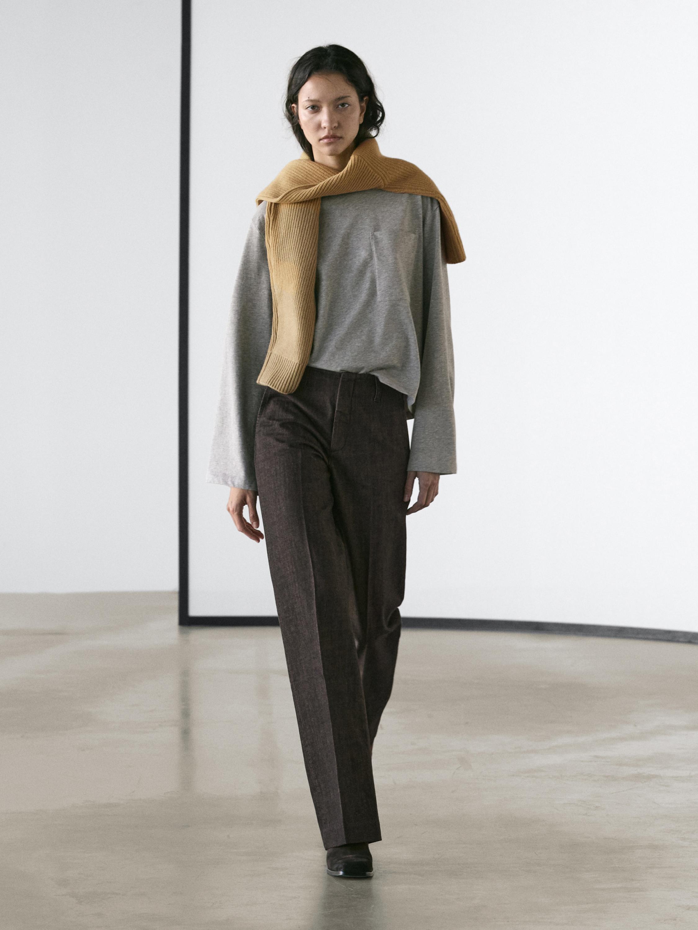 Conjunto de jeans gris natural de pierna ancha y tiro medio, suéter gris y bufanda mostaza sobre los hombros.