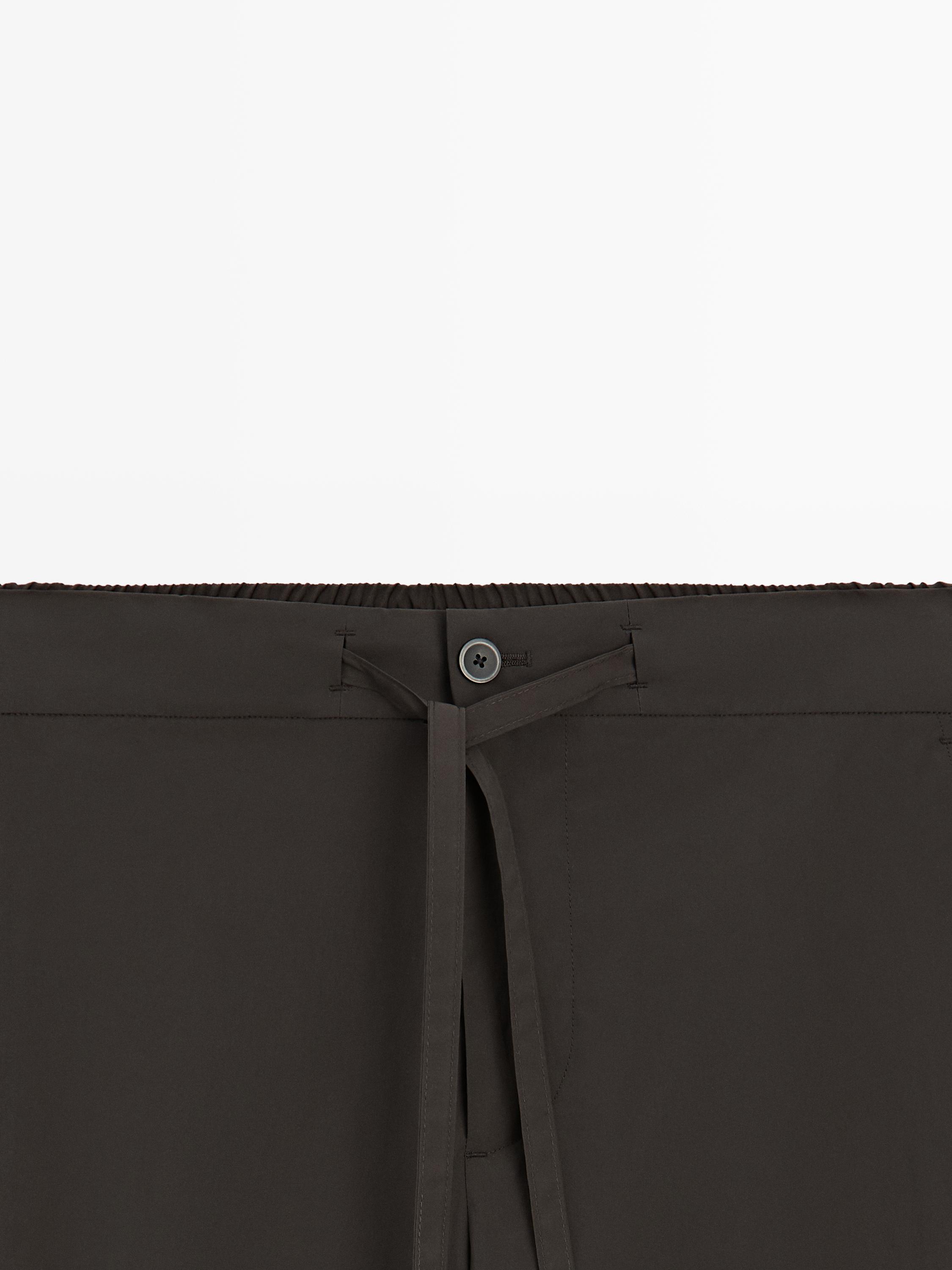 "Detalle de la cintura de pantalón marrón con botón y lazo frontal."
