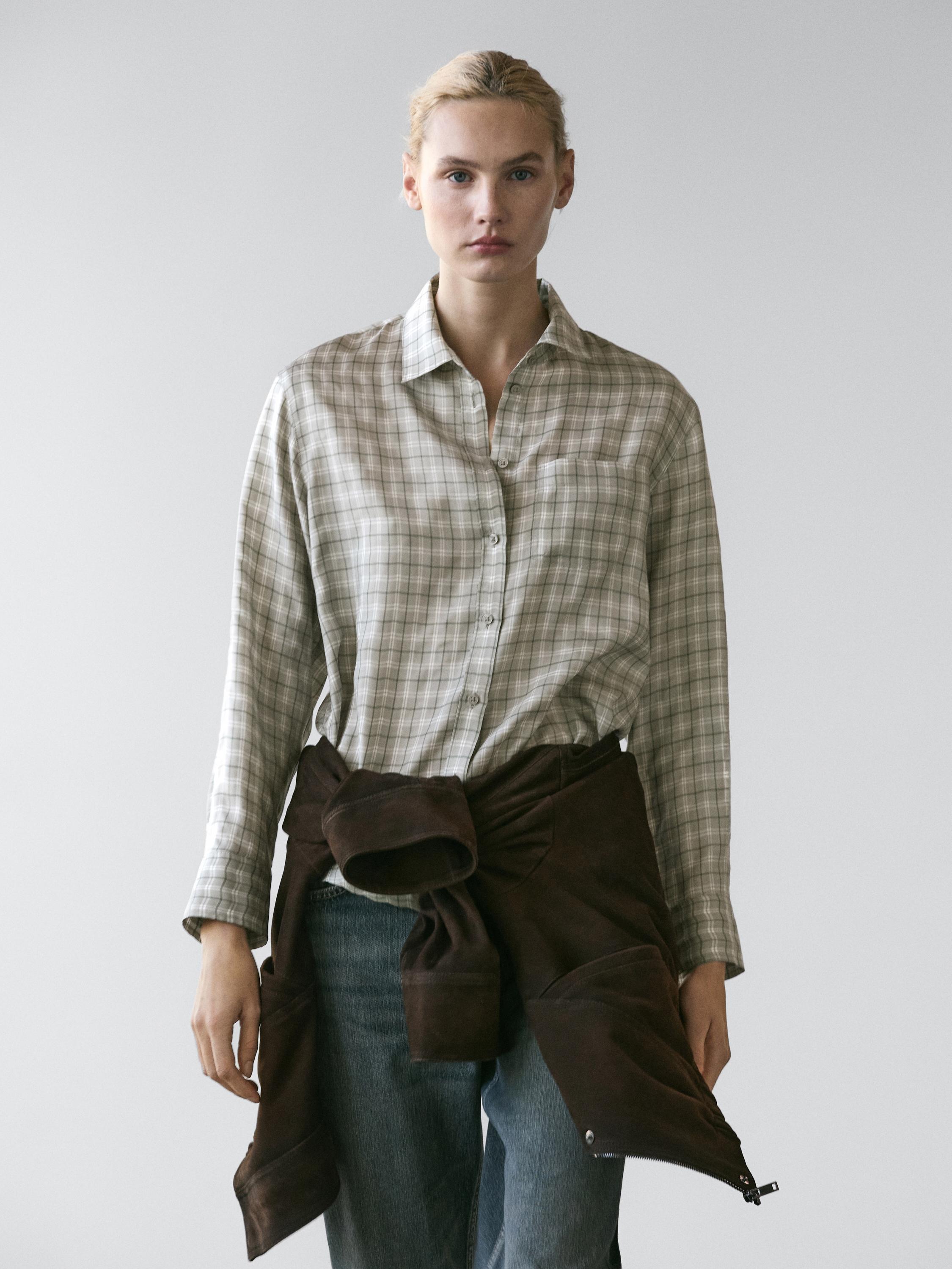 Gray plaid shirt with a chest pocket, brown jacket tied at the waist, and blue jeans.