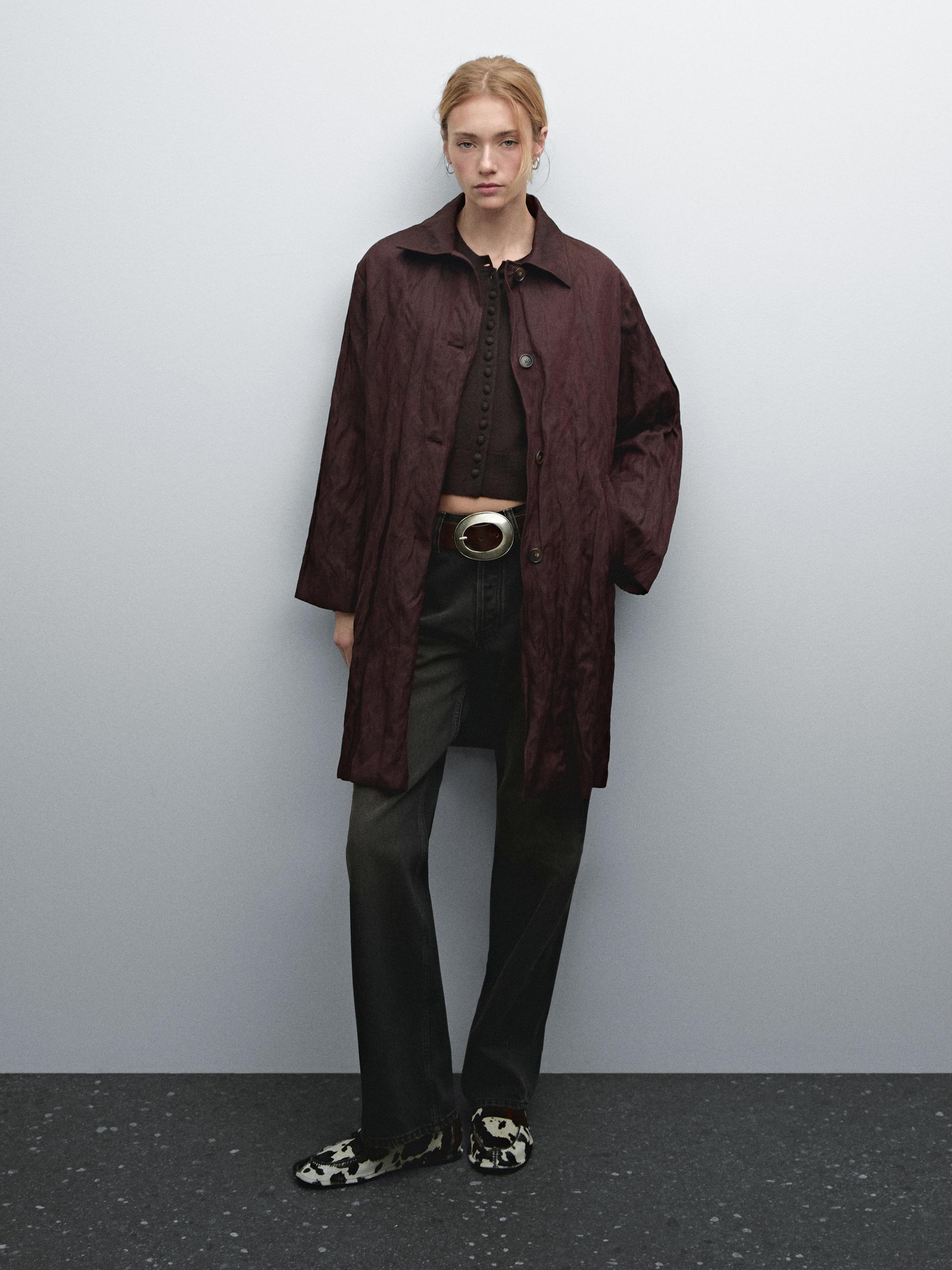 Conjunto de abrigo burdeos, top negro con botones, pantalones oscuros y zapatos estampados.