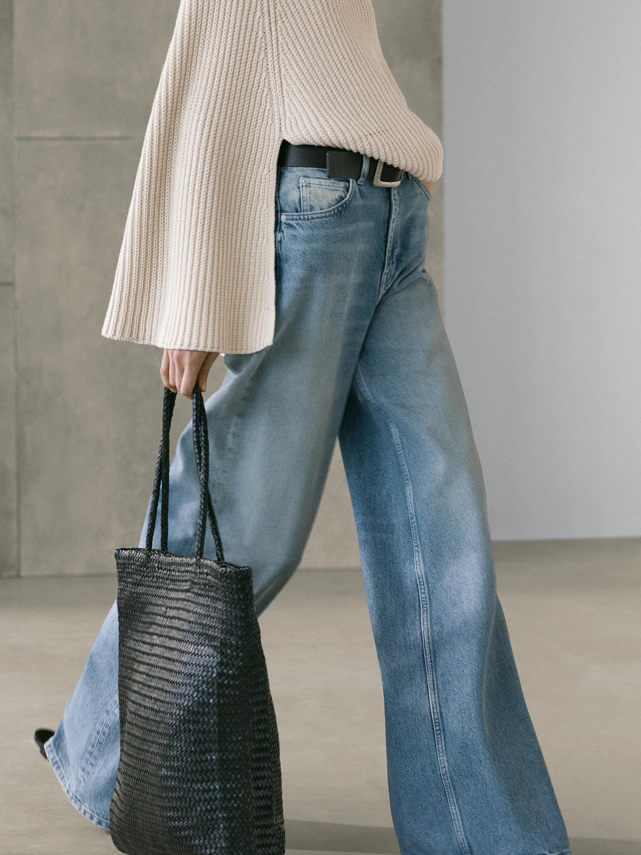 Mellemplan af lyseblå, højtaljede jeans med vide ben, sidelommer og synligt sort bælte.