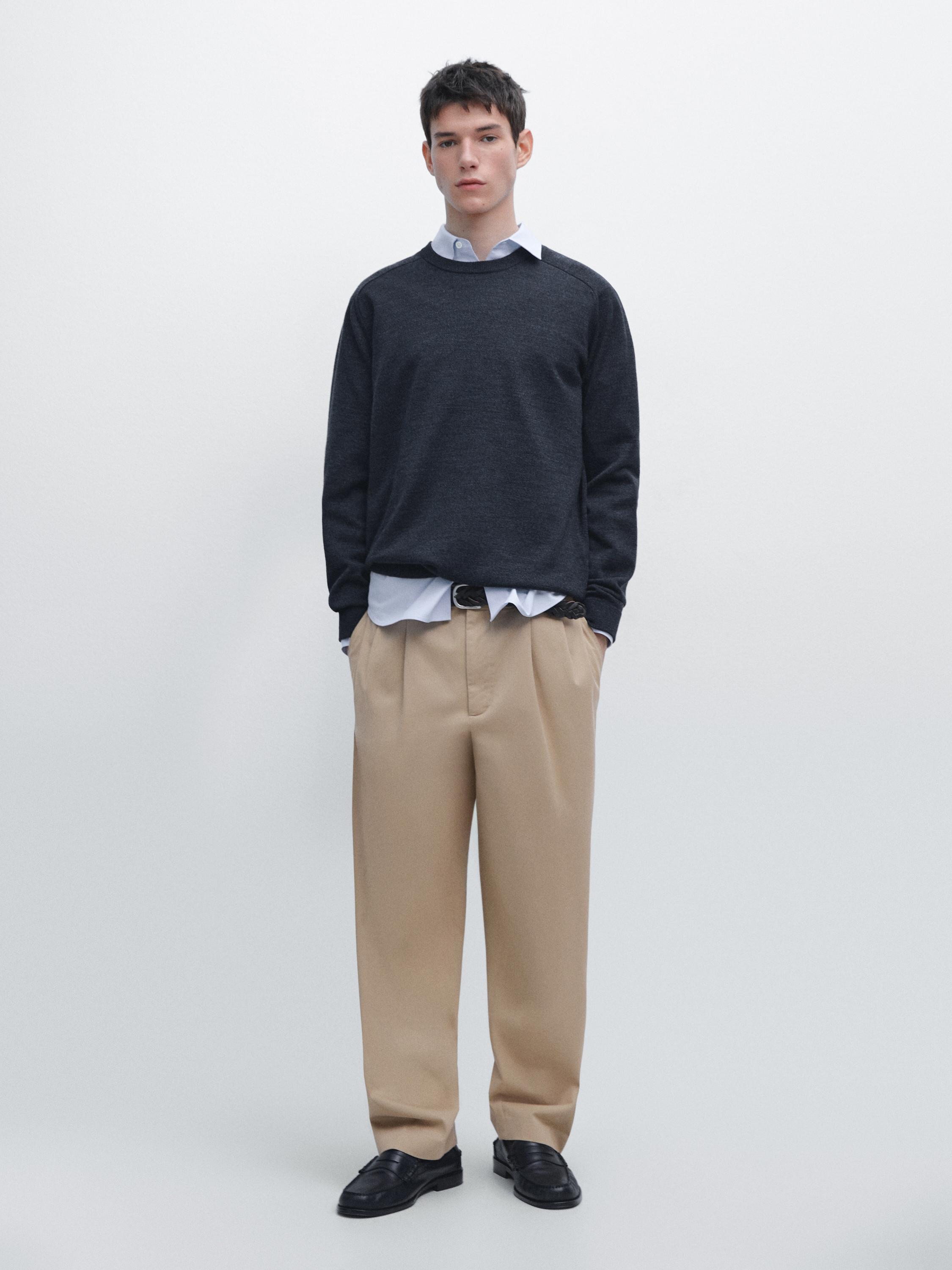 Conjunt de jersei marí fosc de coll rodó, camisa blanca, pantalons beix i mocassins negres.