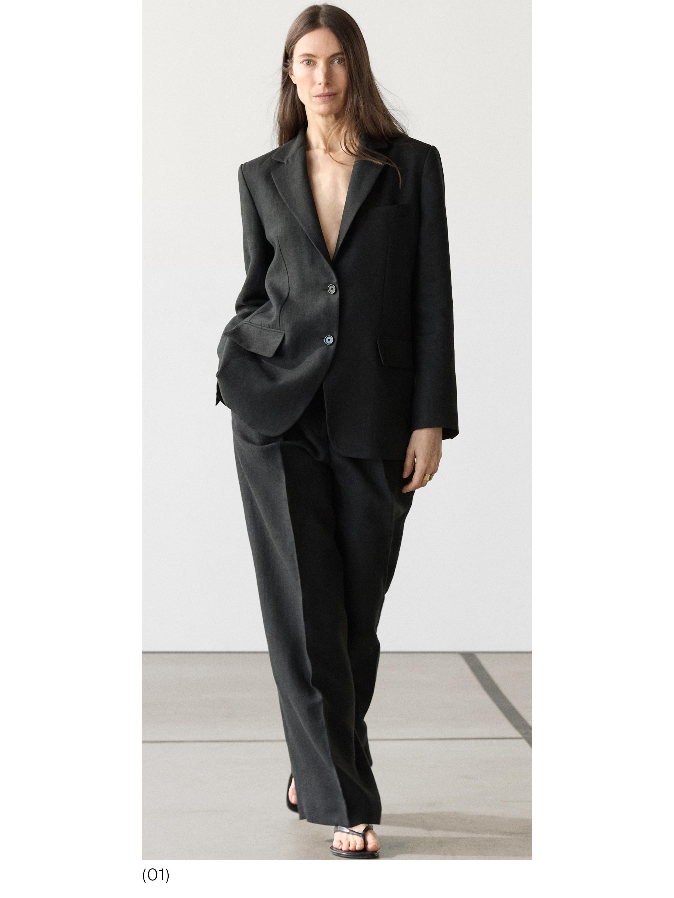 Conjunto de traje negro con blazer de dos botones y bolsillos con solapa, pantalones anchos y sandalias negras.