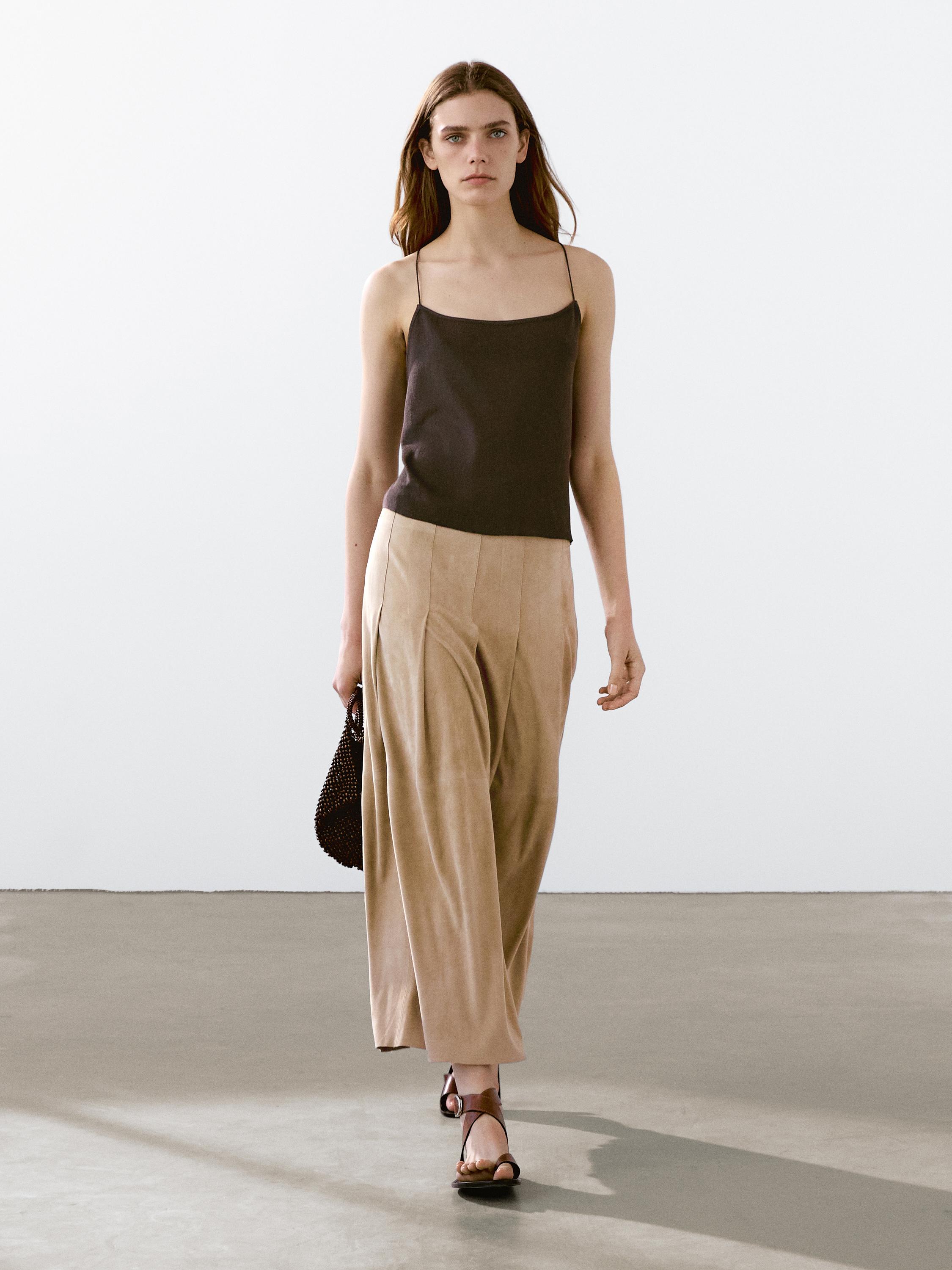 طقم يتكون من توب أسود بحمالات رفيعة وبنطلون بيج فضفاض، وصندل بني.