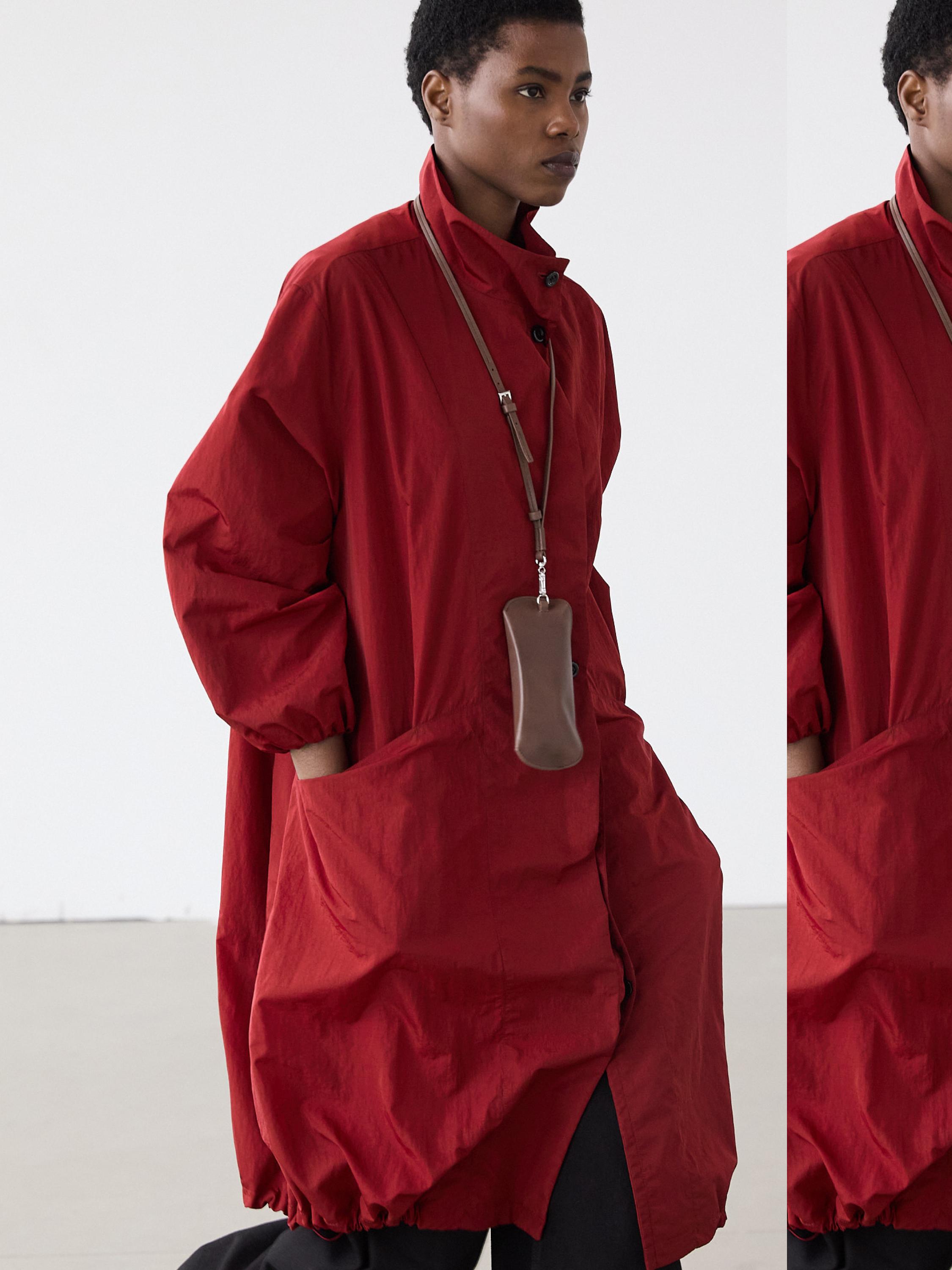 Plano medio de parka roja larga oversize con bolsillos laterales y cierre de botones.