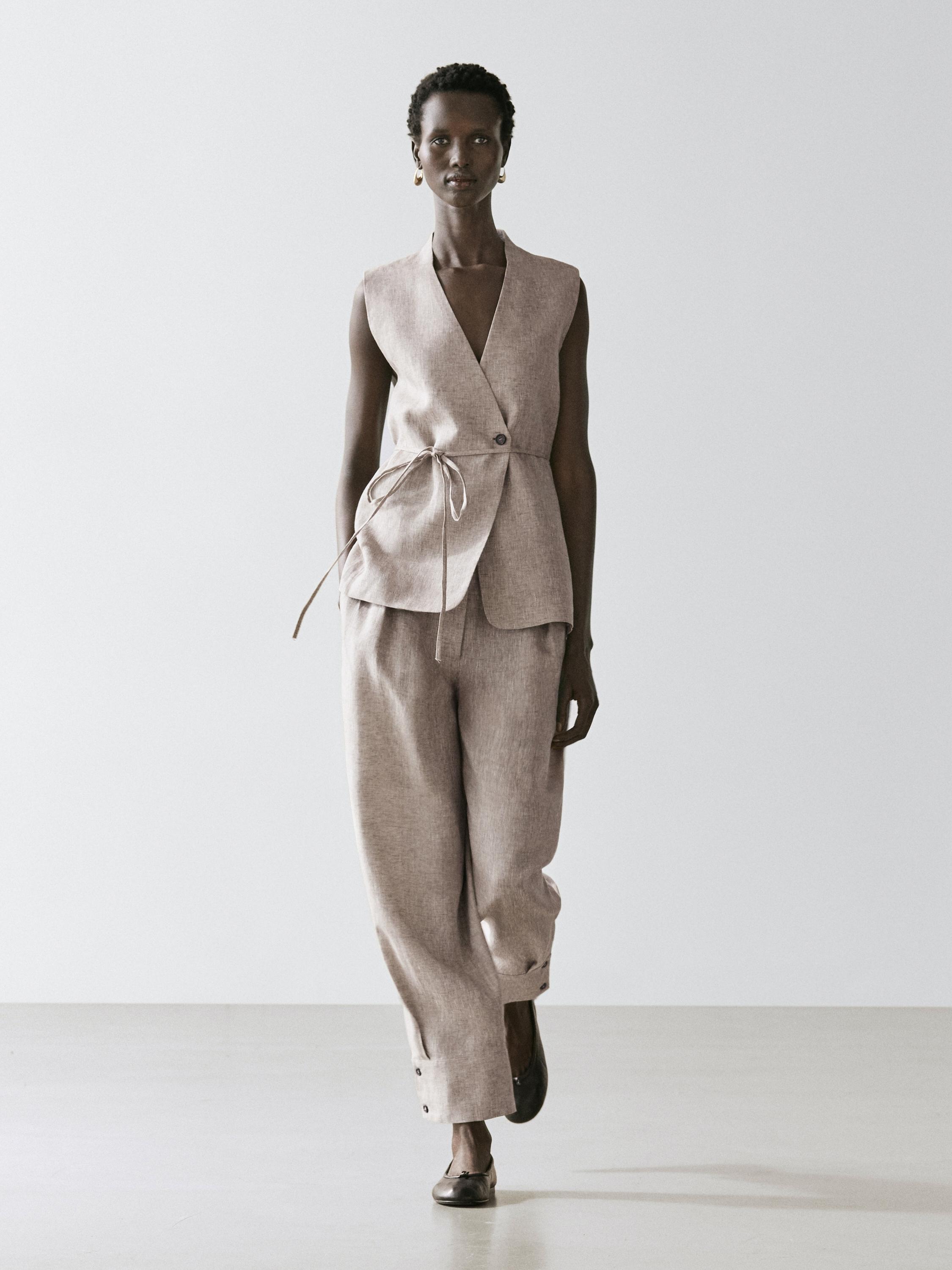 Conjunto de chaleco beige sin mangas con cinturón y pantalones anchos a juego, botón visible en el dobladillo.