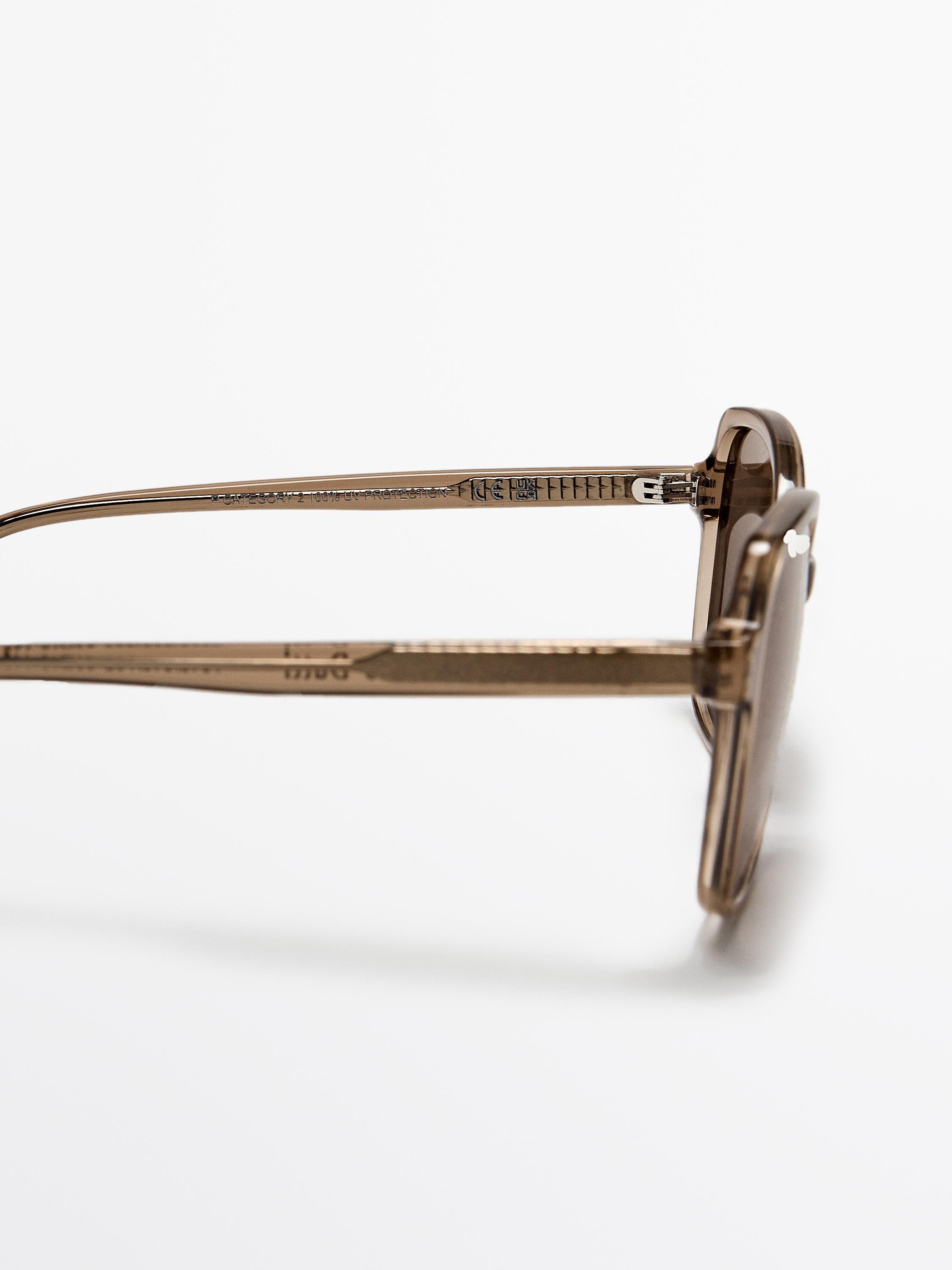 Caramelu koloreko eguzkitako betaurrekoen xehetasuna, alboko ikuspegia grabatutako testua duten patillak erakusten.