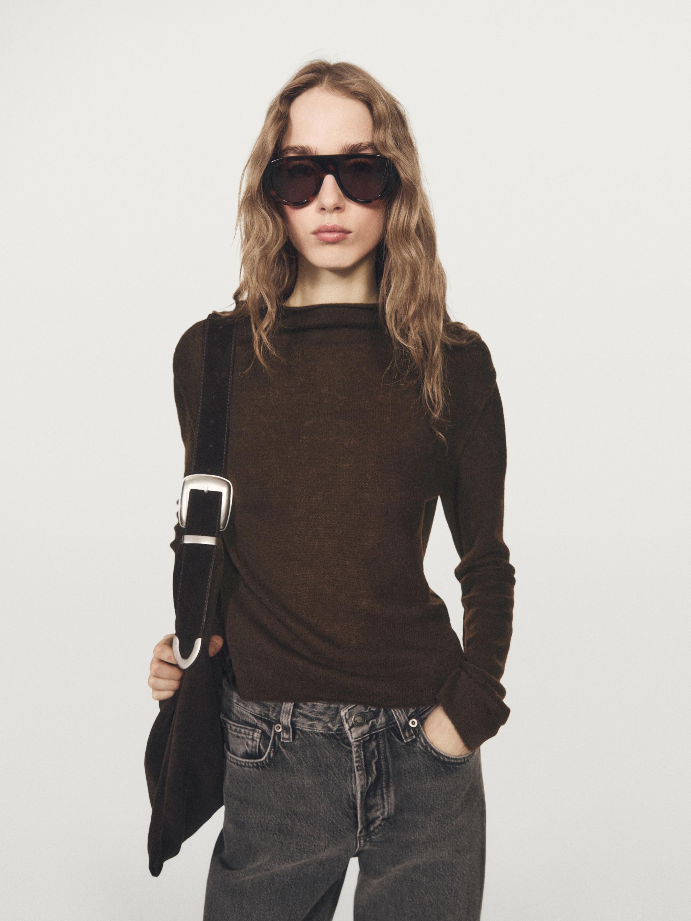 Plan moyen d'un pull marron en maille avec col roulé, combiné avec un jean foncé et un sac noir.