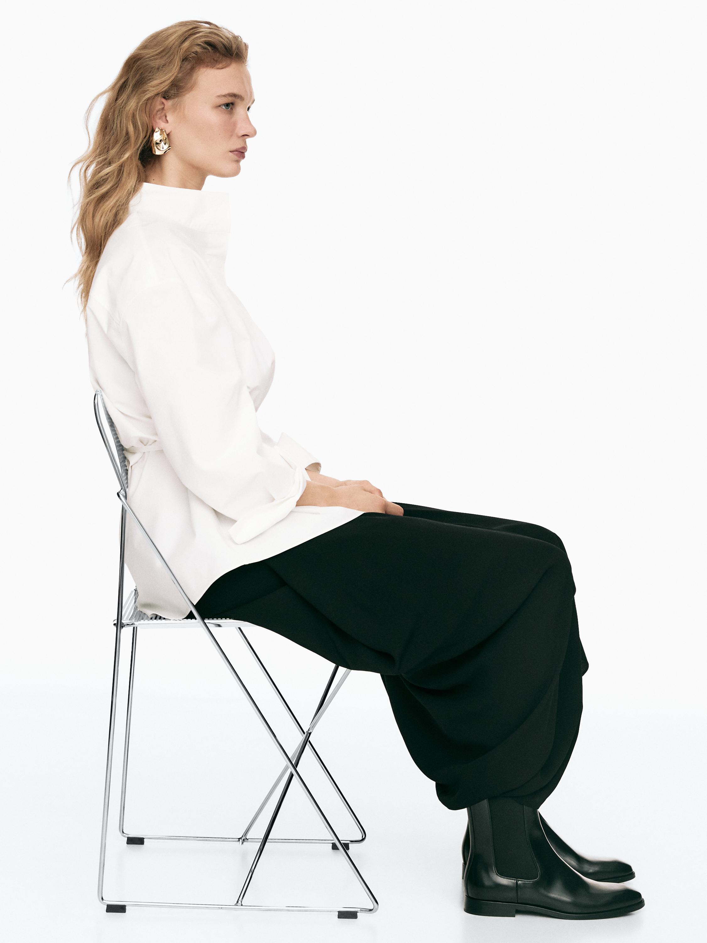 Ensemble composé d'un chemisier blanc à col roulé, d'un pantalon noir ample et de bottines noires montantes.