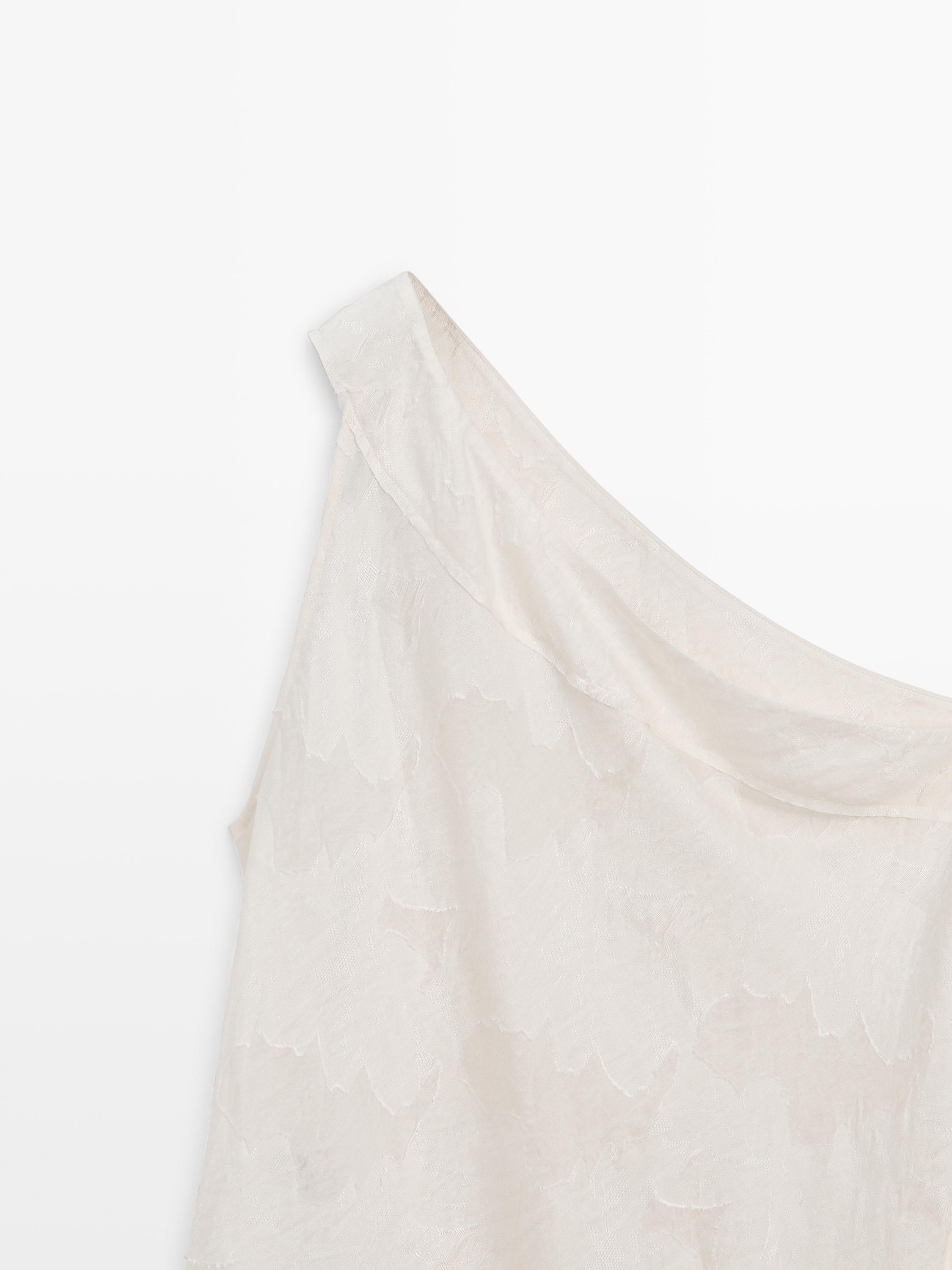 Λεπτομέρεια ασύμμετρης λαιμόκοψης λευκού τοπ με διακριτική υφή.