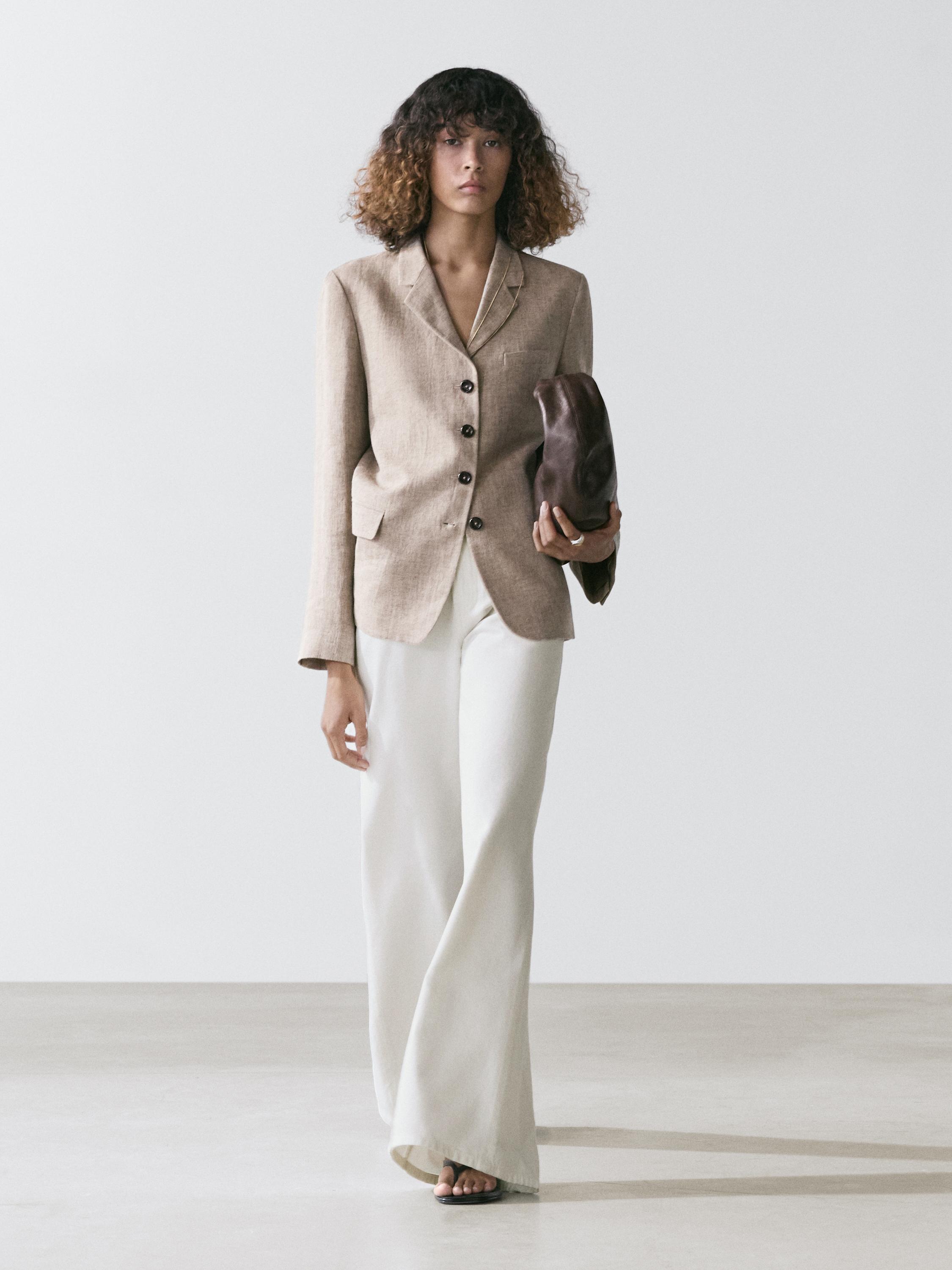 Ensemble blazer beige avec boutons foncés et poches à rabat, assorti à un pantalon blanc à jambes larges.