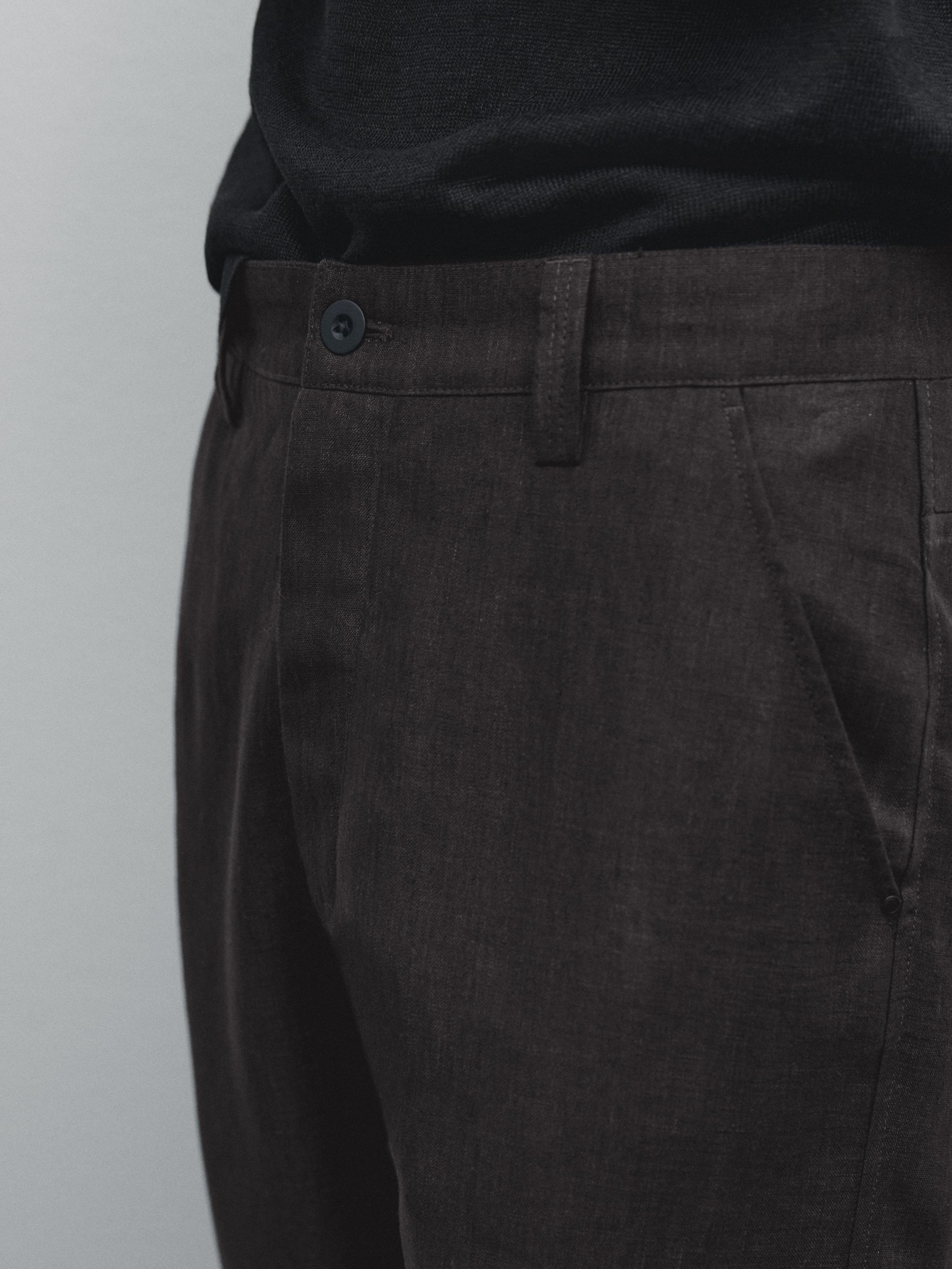 Gros plan sur un pantalon foncé avec bouton et poches latérales.
