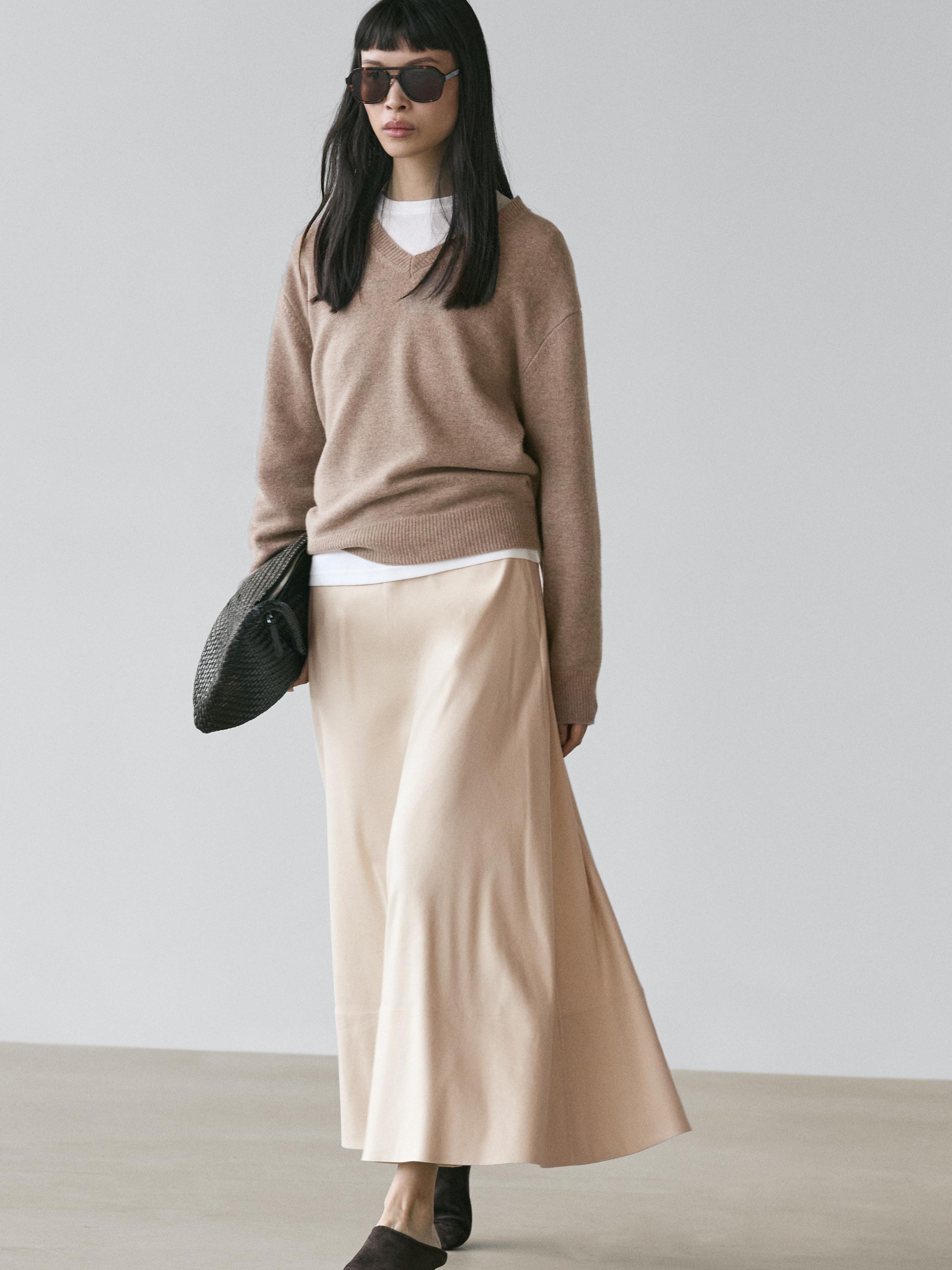 Raw long flared skirt set with pockets and brown V-neck sweater over white t-shirt.