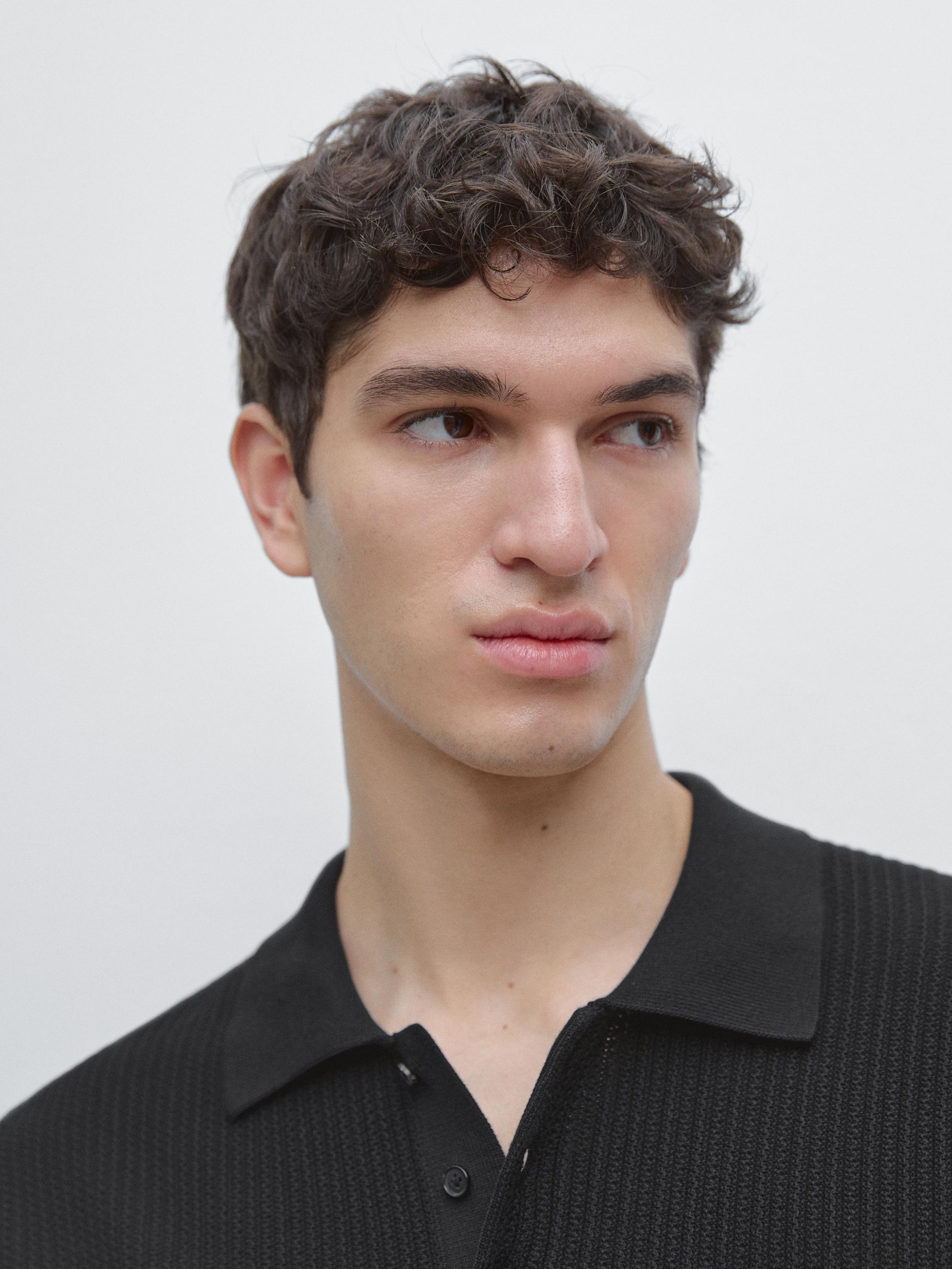 لقطة مقربة لقميص بولو أسود محبوك بياقة كلاسيكية وأزرار جزئية.